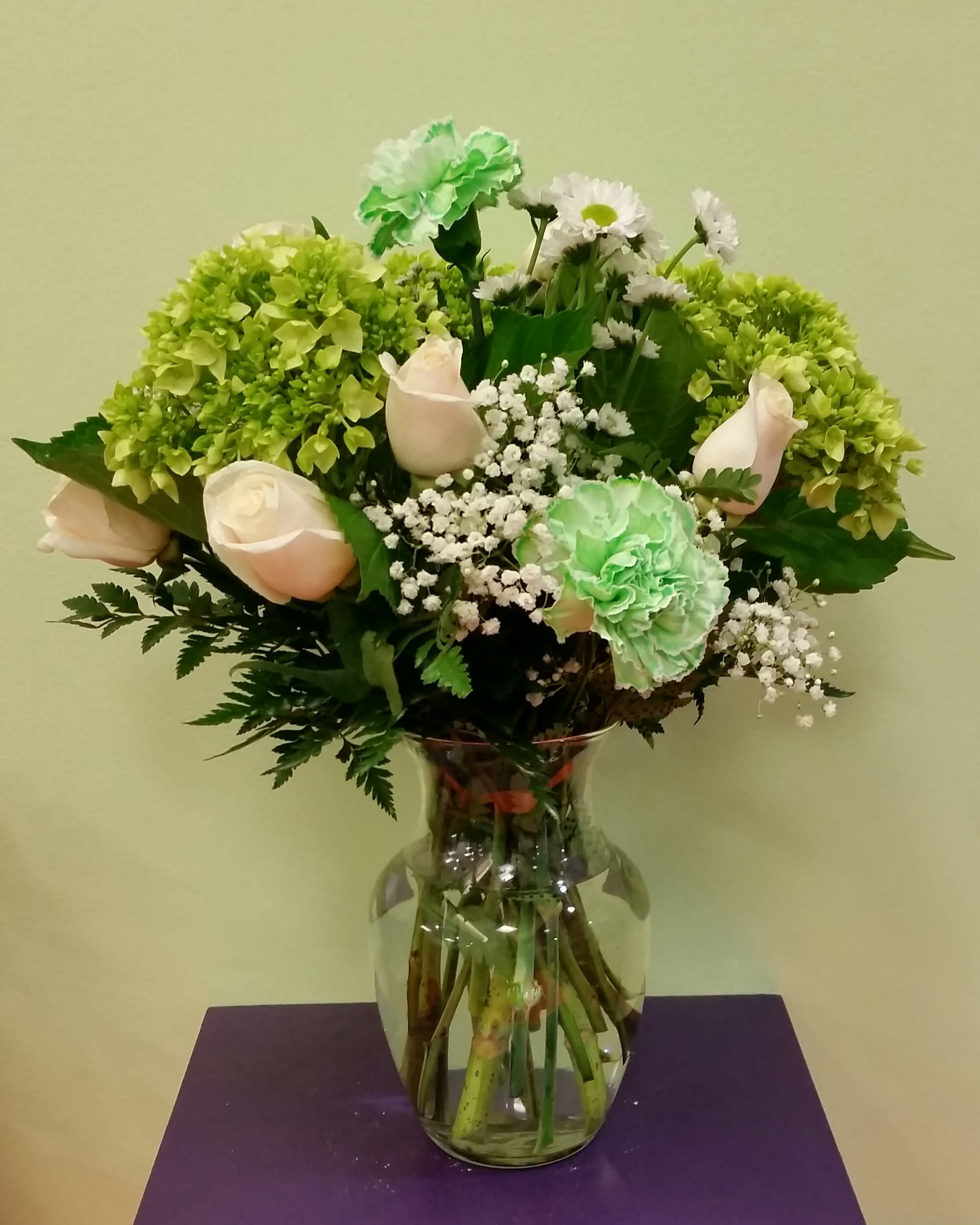 Bouquet of pale roses, green carnations, and white daisies in a glass vase