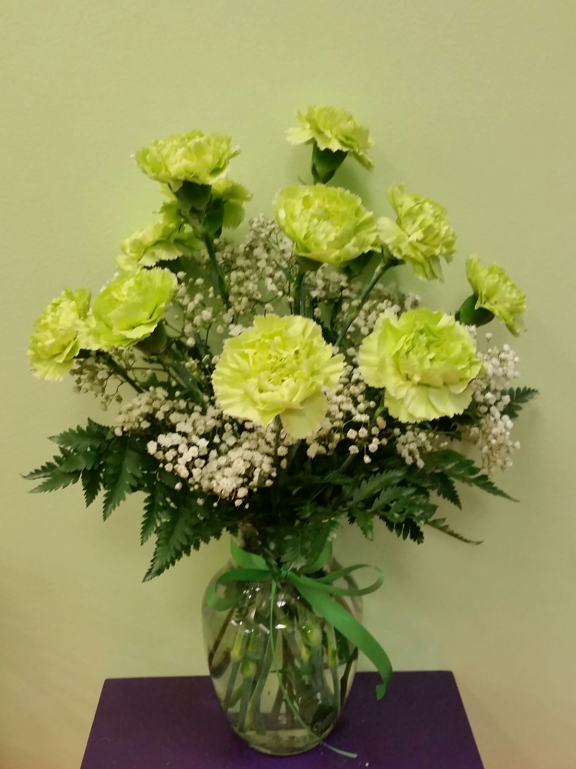 Green carnations and baby's breath in a glass vase with a ribbon