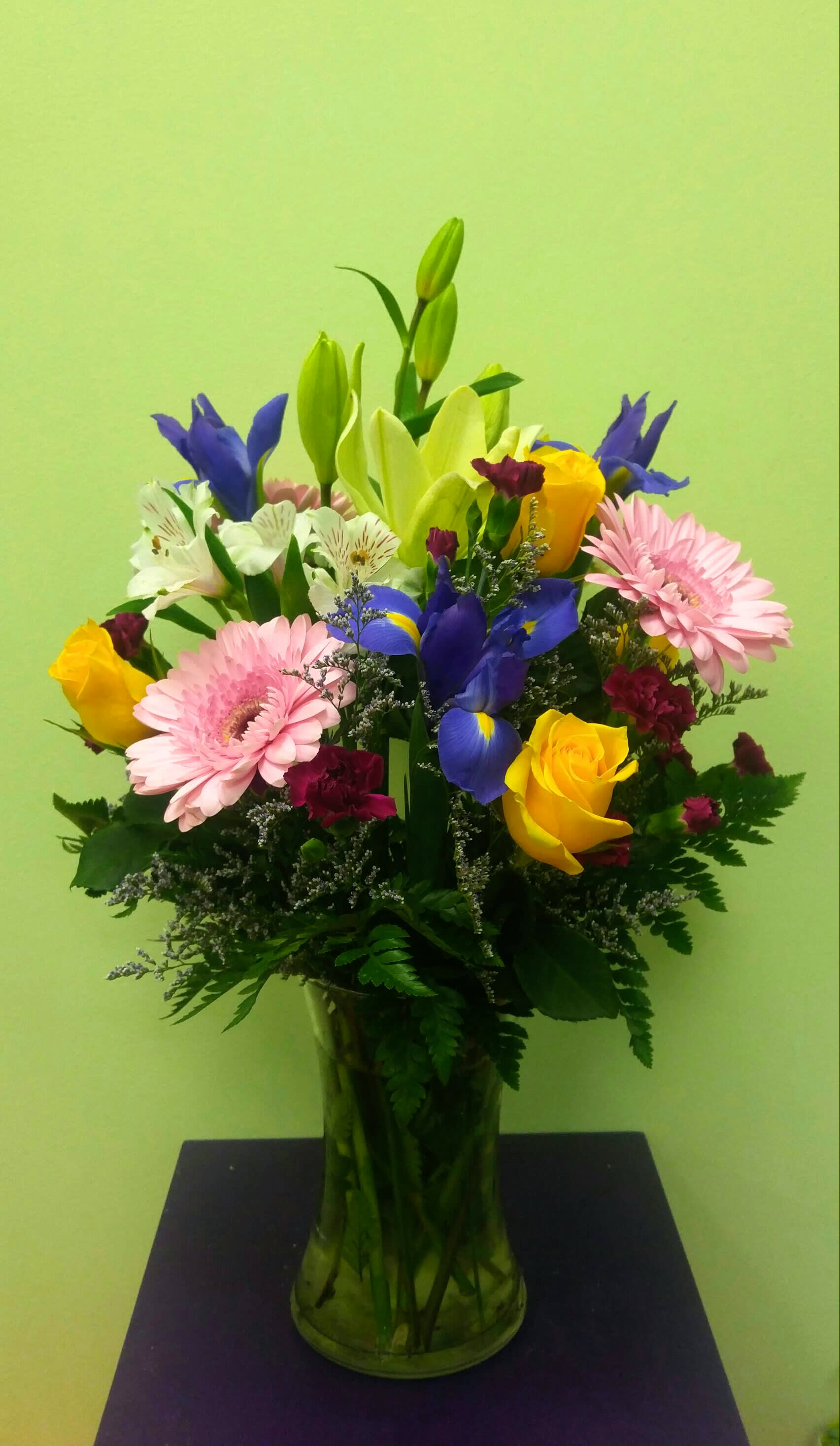 Mixed bouquet of lilies, roses, irises, and gerbera daisies in a glass vase