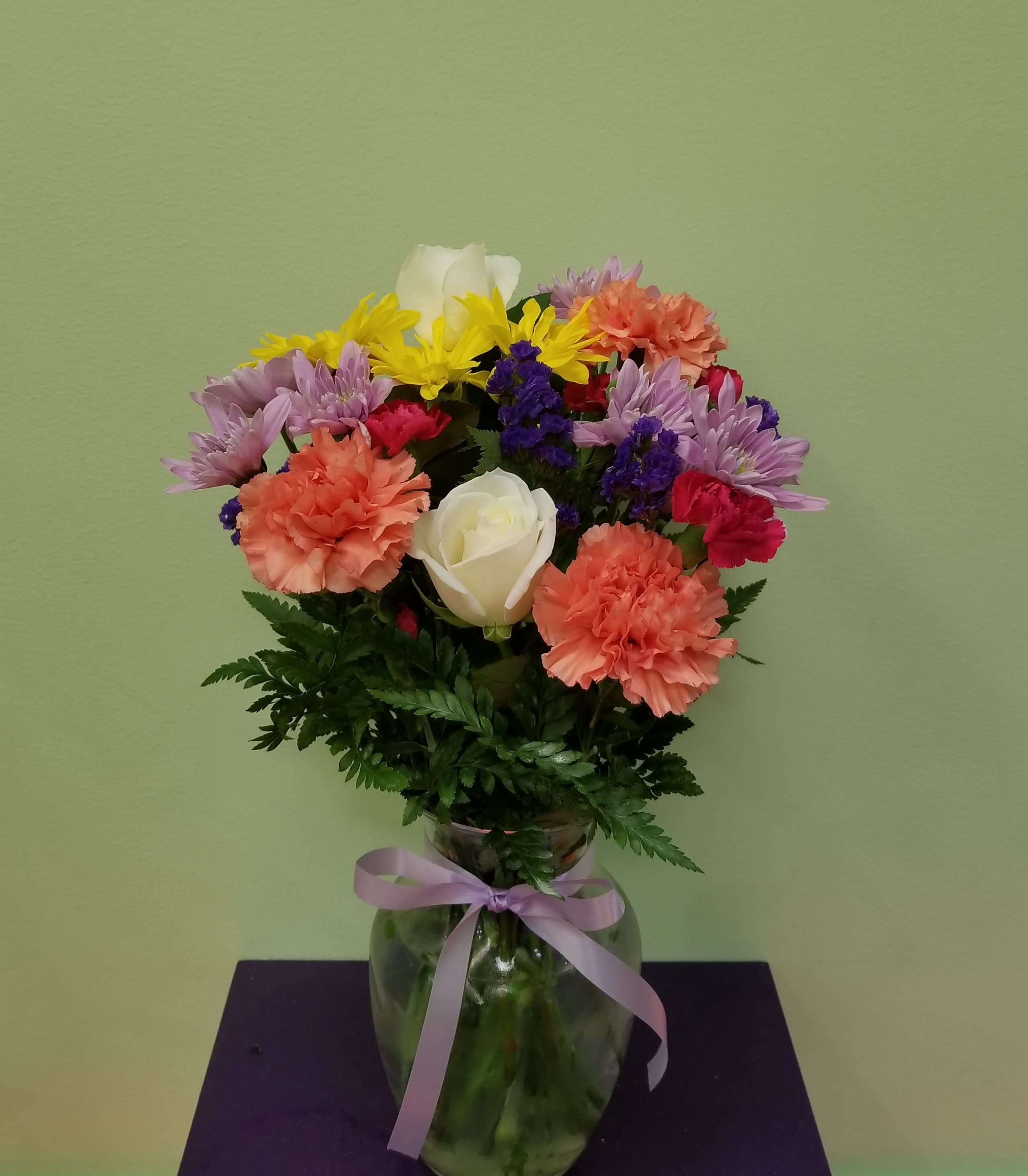 Mixed bouquet of carnations, daisies, and roses in a glass vase with a ribbon