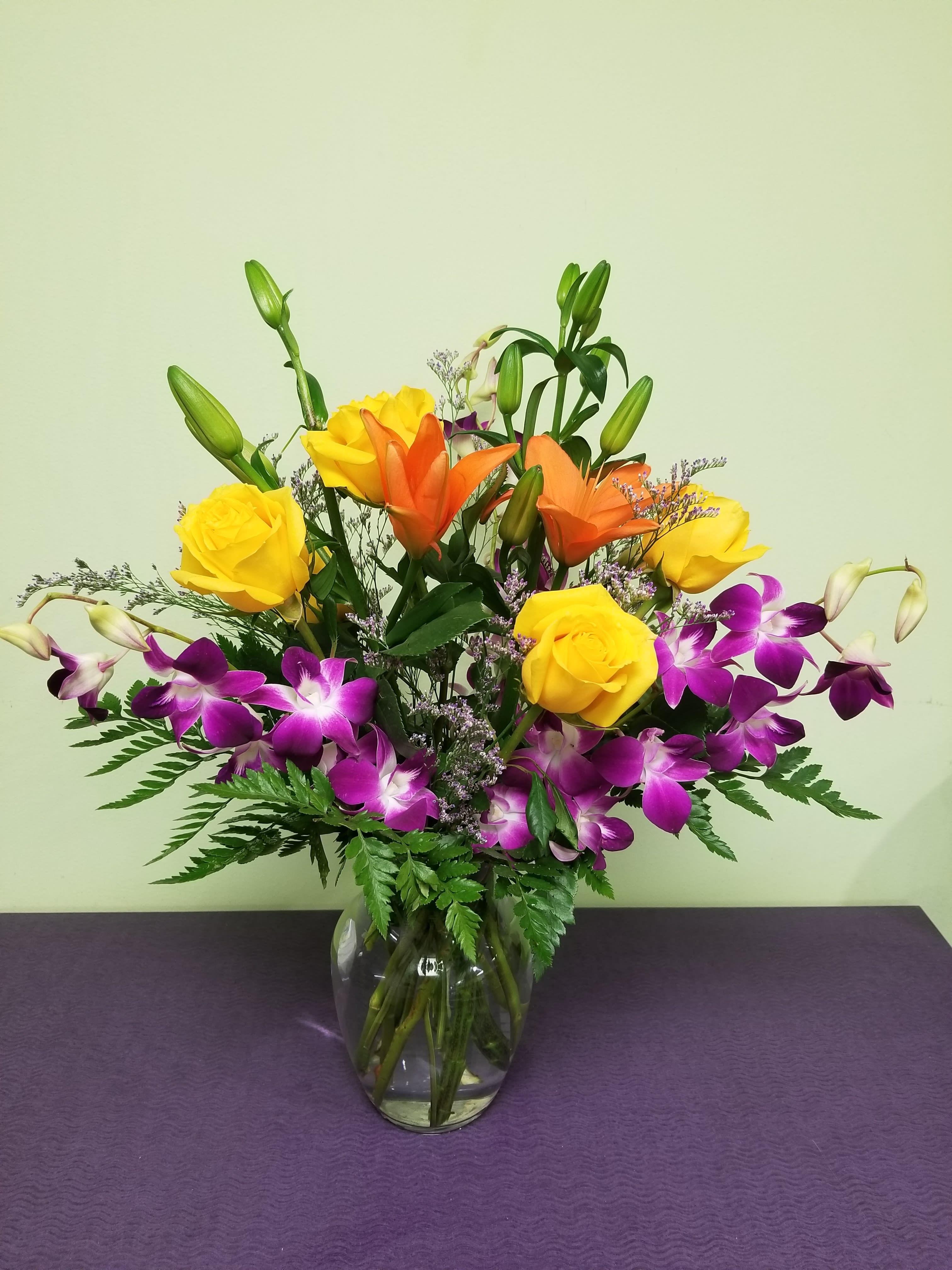 Mixed bouquet of yellow roses, orange lilies, and purple orchids in a glass vase