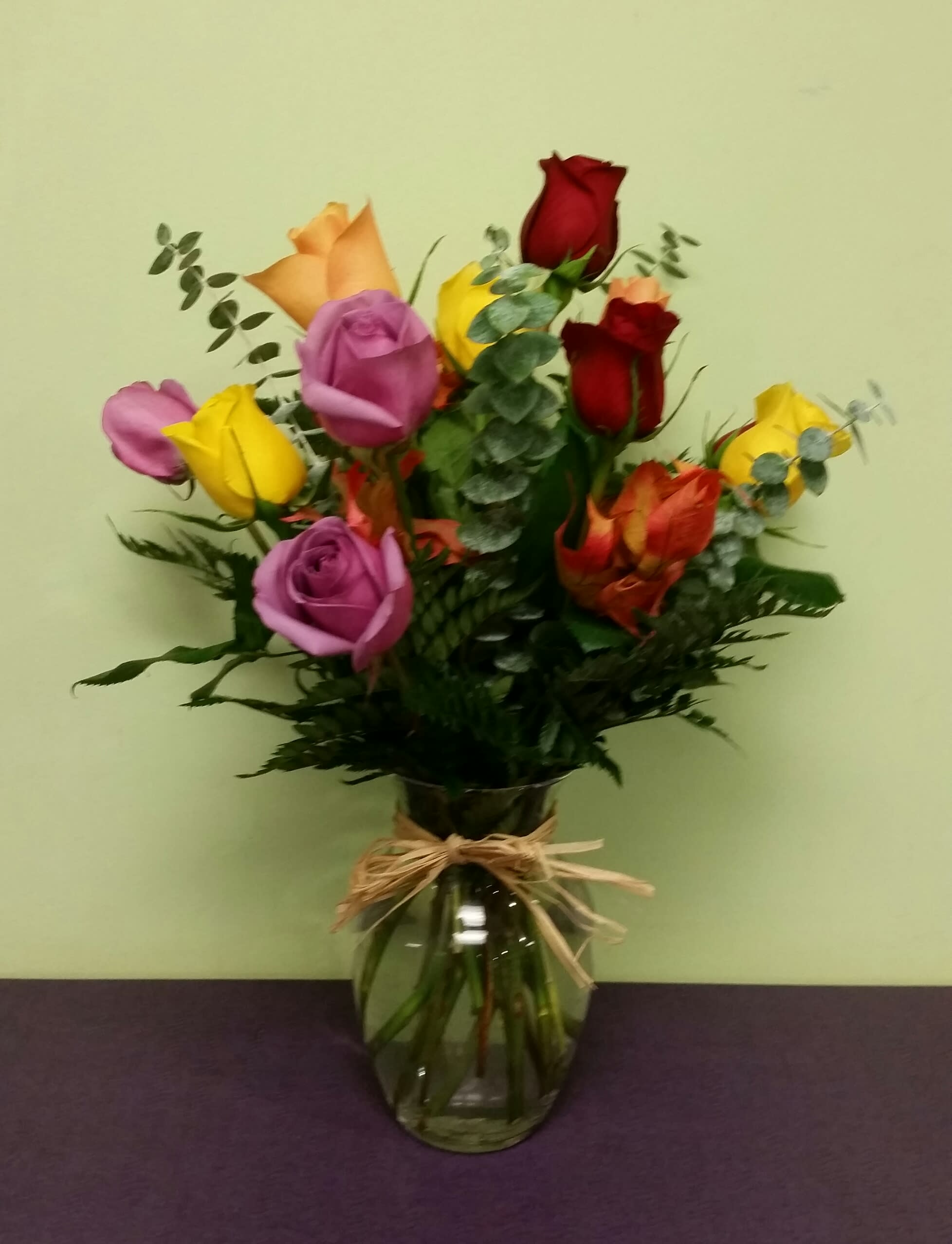 Bouquet of multicolored roses in a glass vase with a raffia bow
