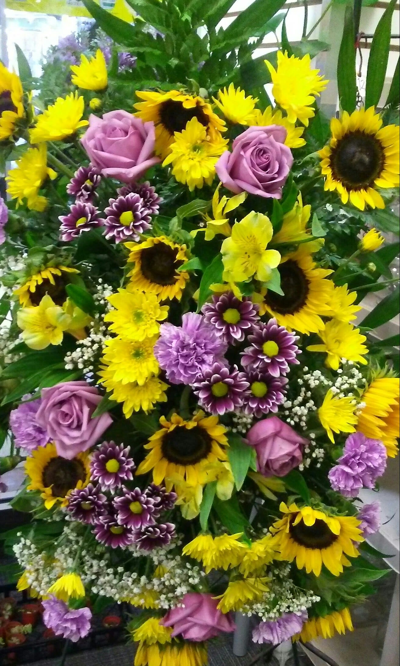 Bouquet of yellow sunflowers, purple roses, and purple daisies