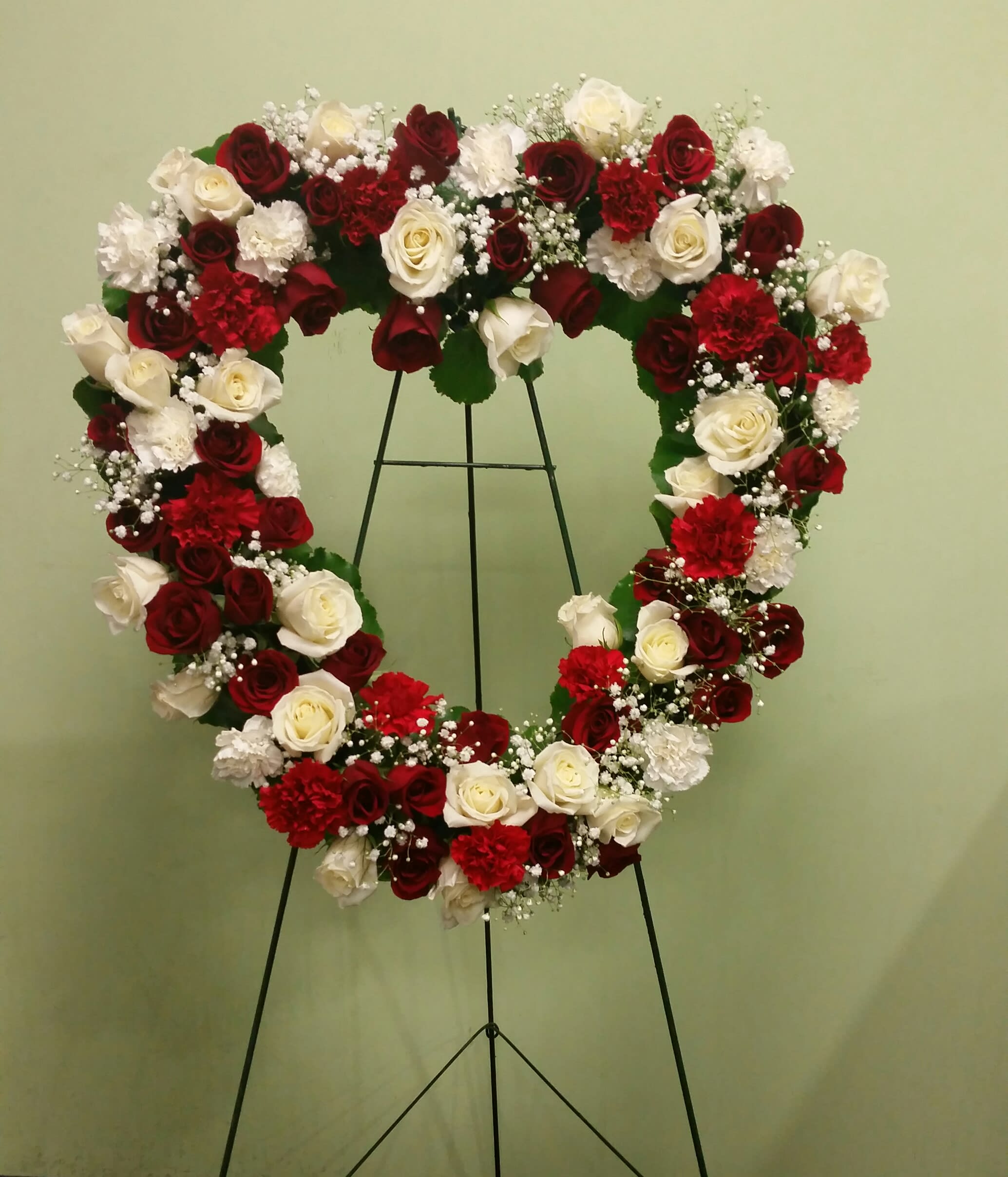 Heart-shaped floral wreath of red and white roses on a stand