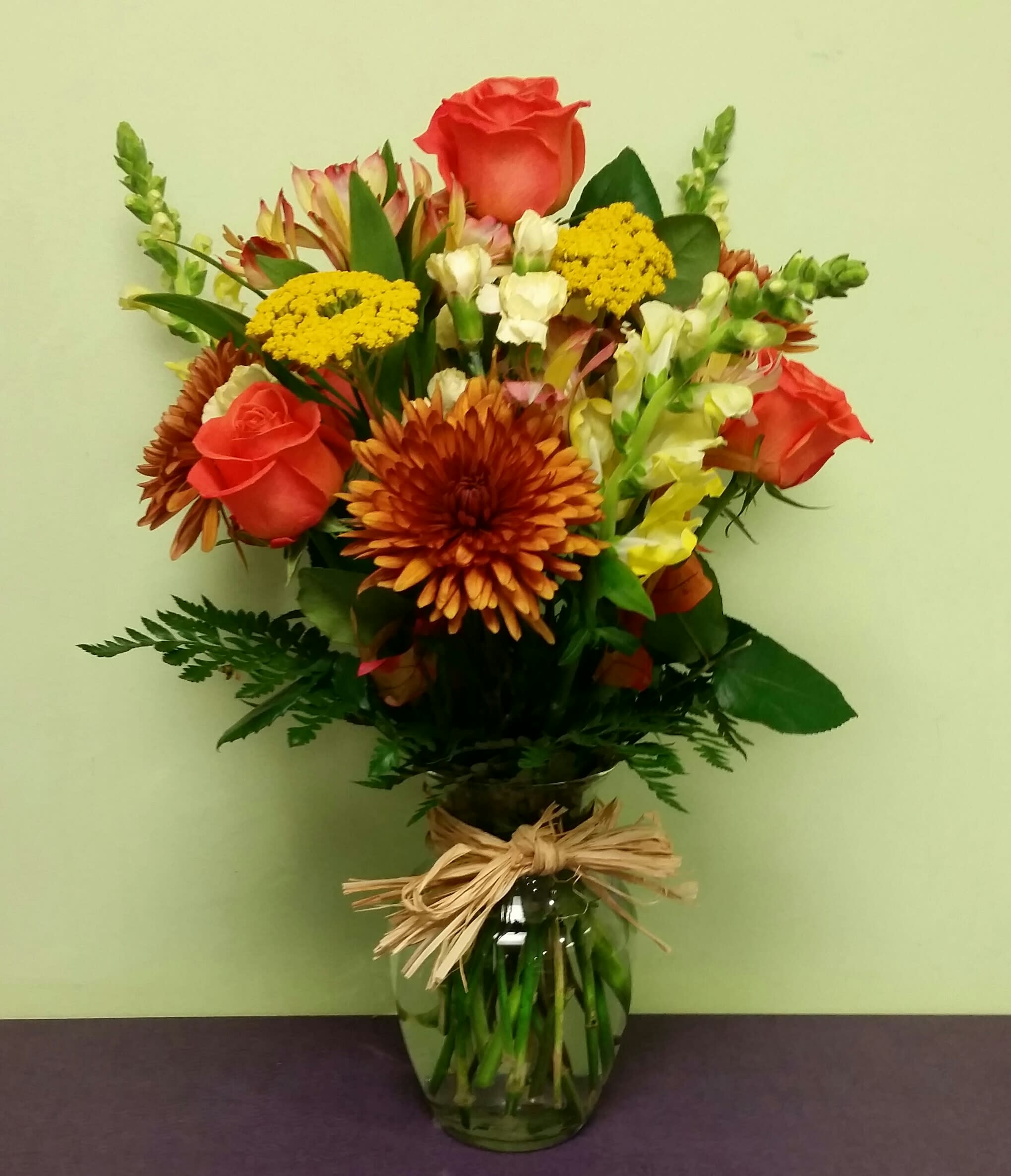 Mixed bouquet of orange roses, yellow blooms, and chrysanthemums in a glass vase