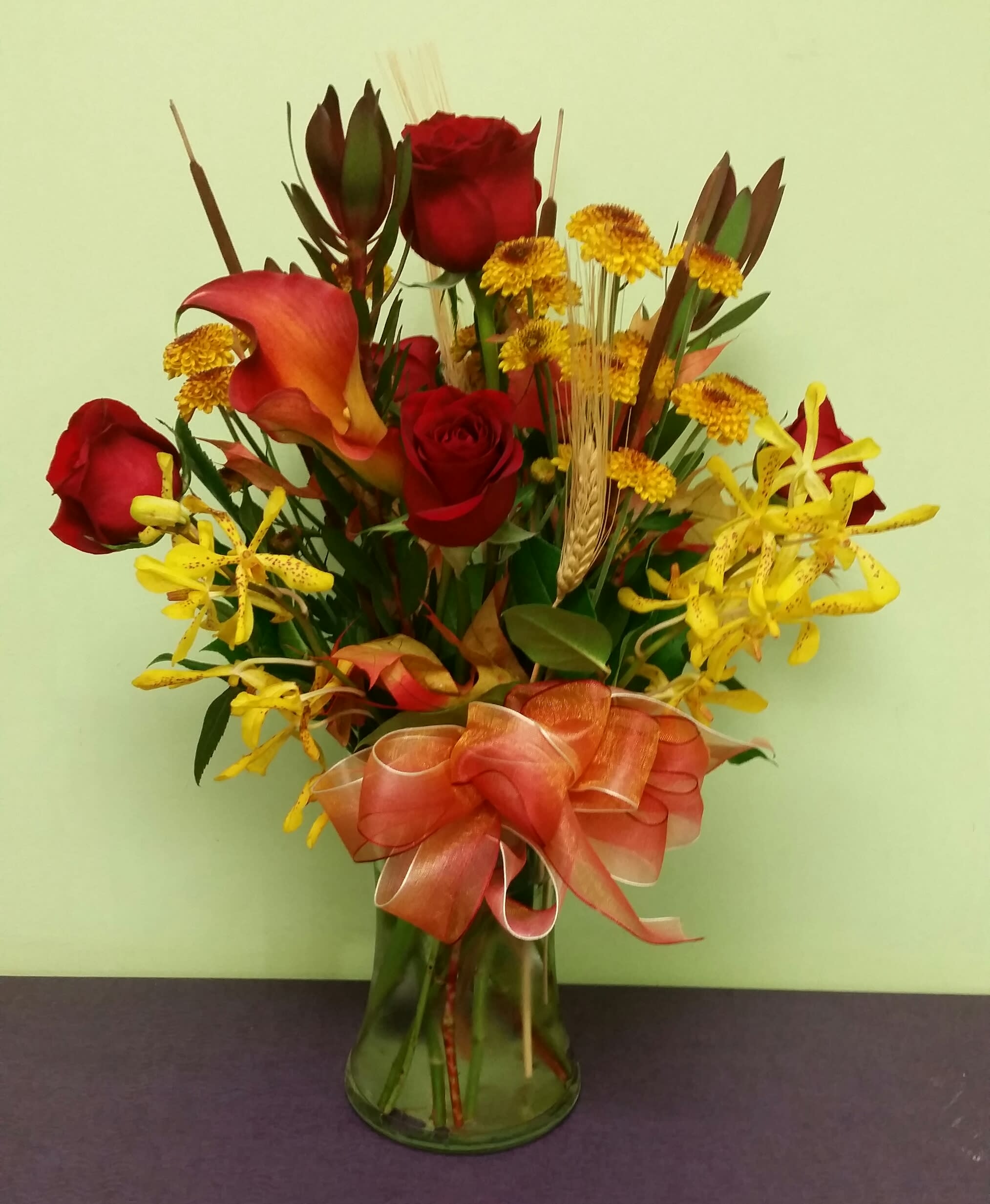 Bouquet of red roses, yellow orchids, and calla lilies in a glass vase