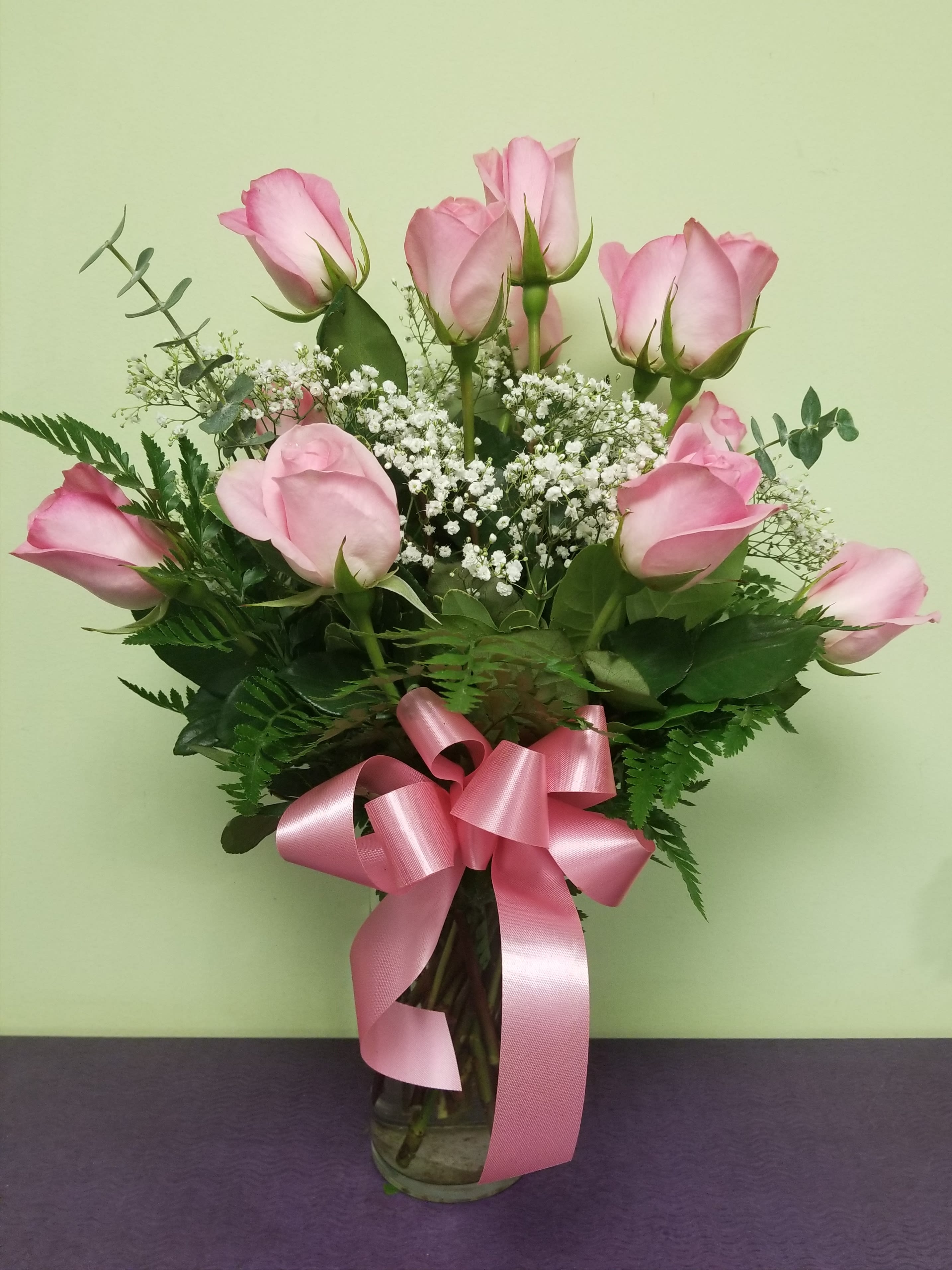 Pink roses in a glass vase with baby's breath and a pink ribbon