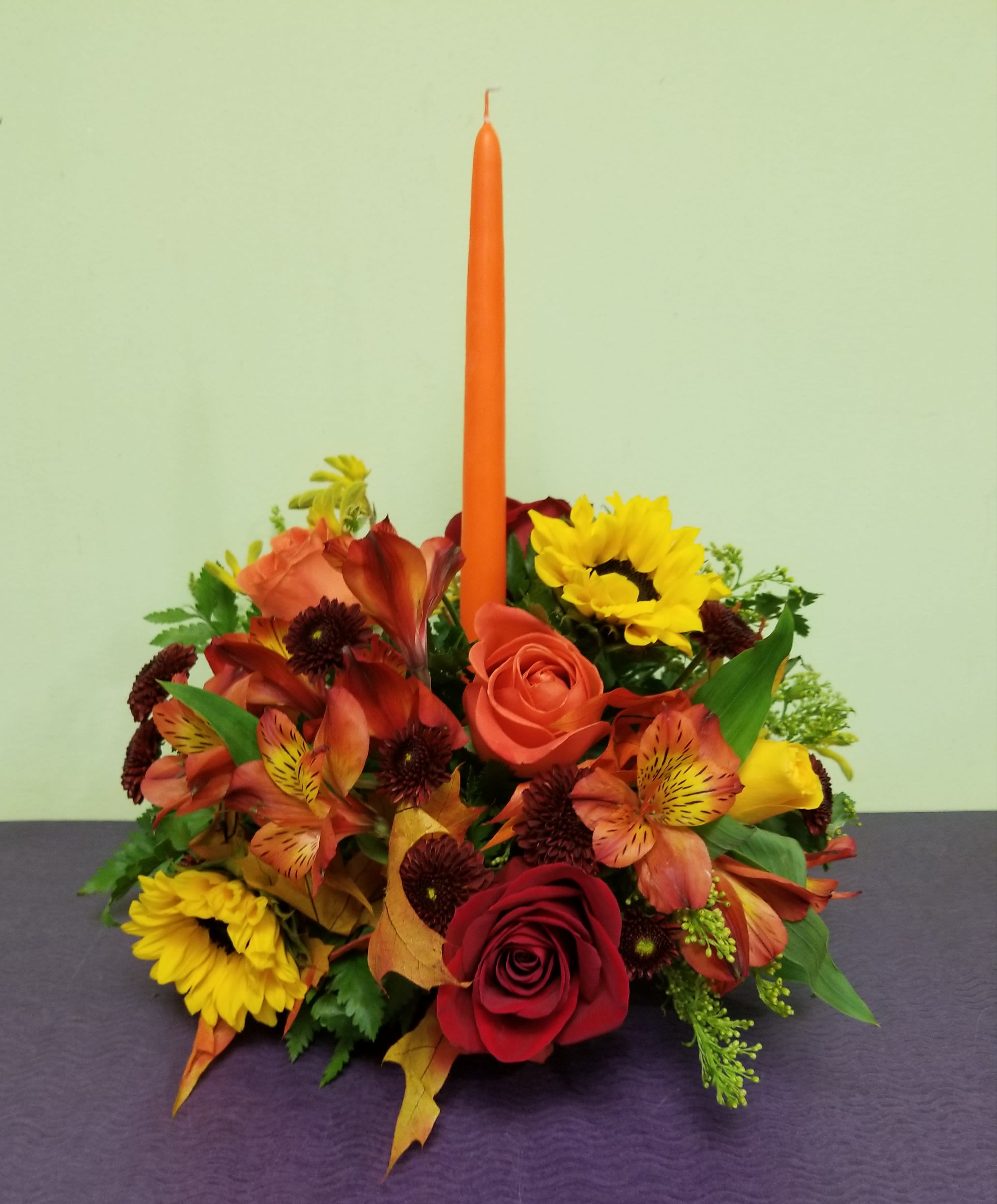 Autumn floral centerpiece with roses, sunflowers, and a tall orange candle
