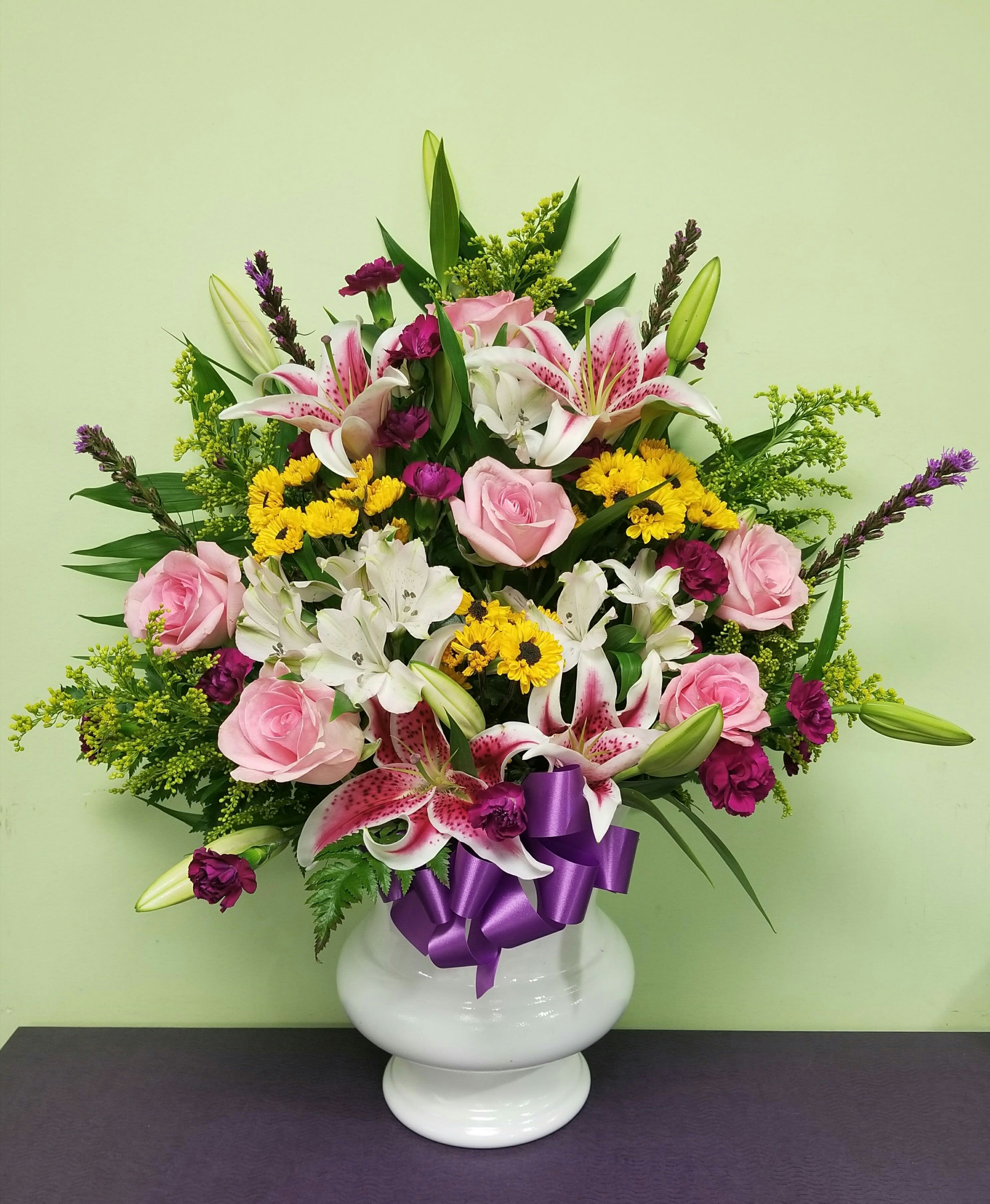 Pink roses and lilies in a white vase with a purple ribbon