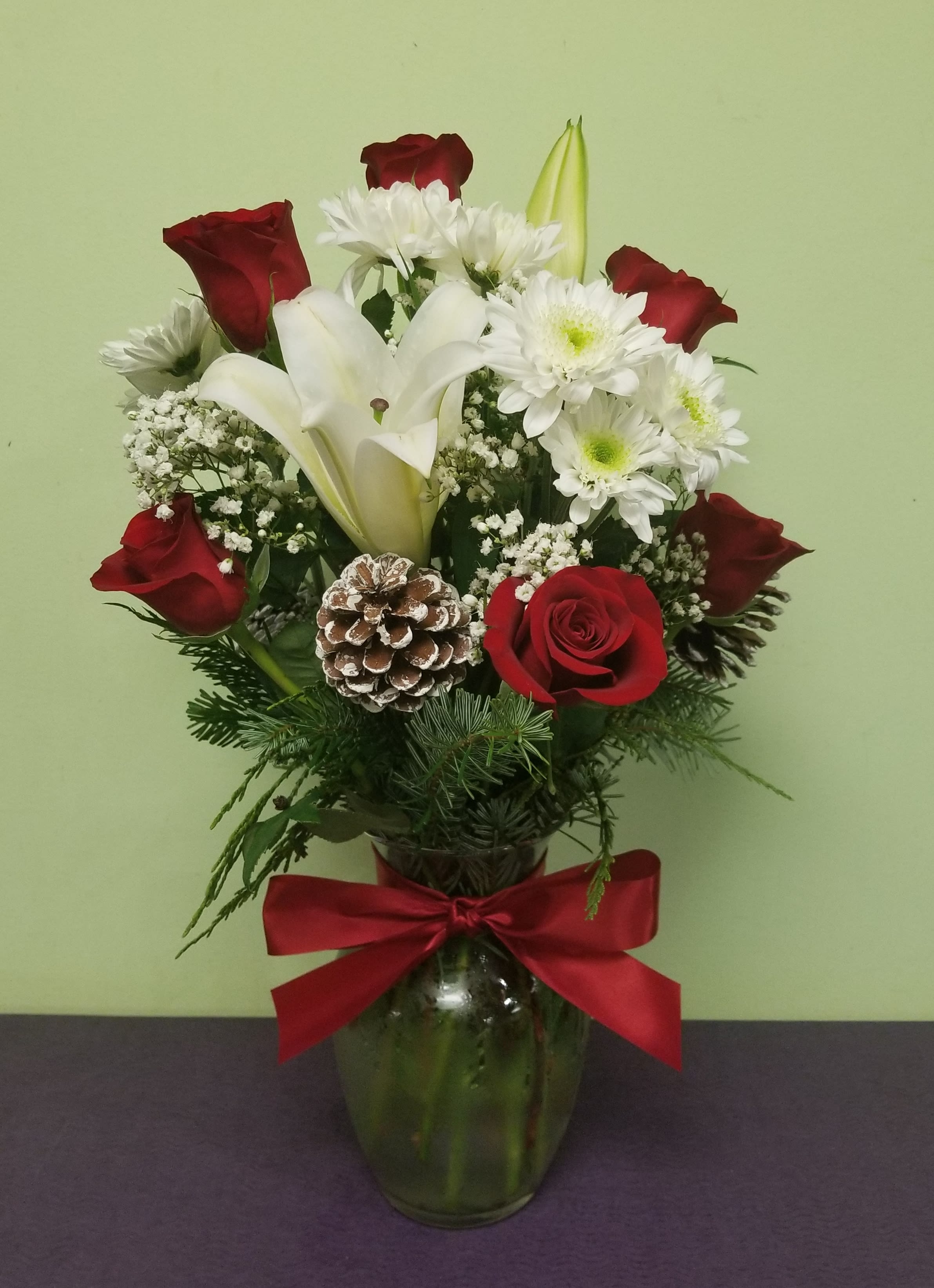 Red roses and white lilies in a glass vase with a red bow