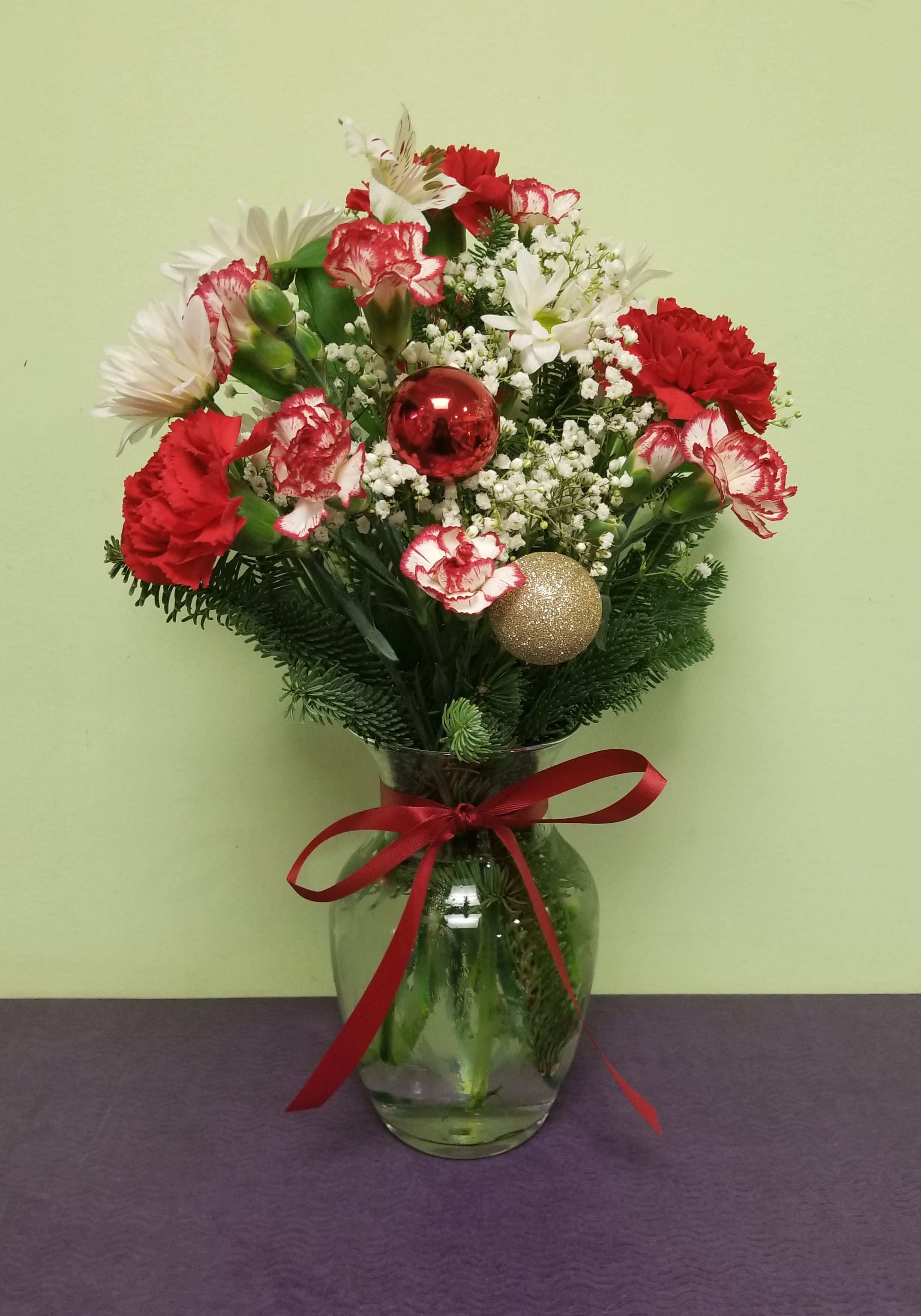 Red and white floral arrangement in a glass vase with holiday ornaments