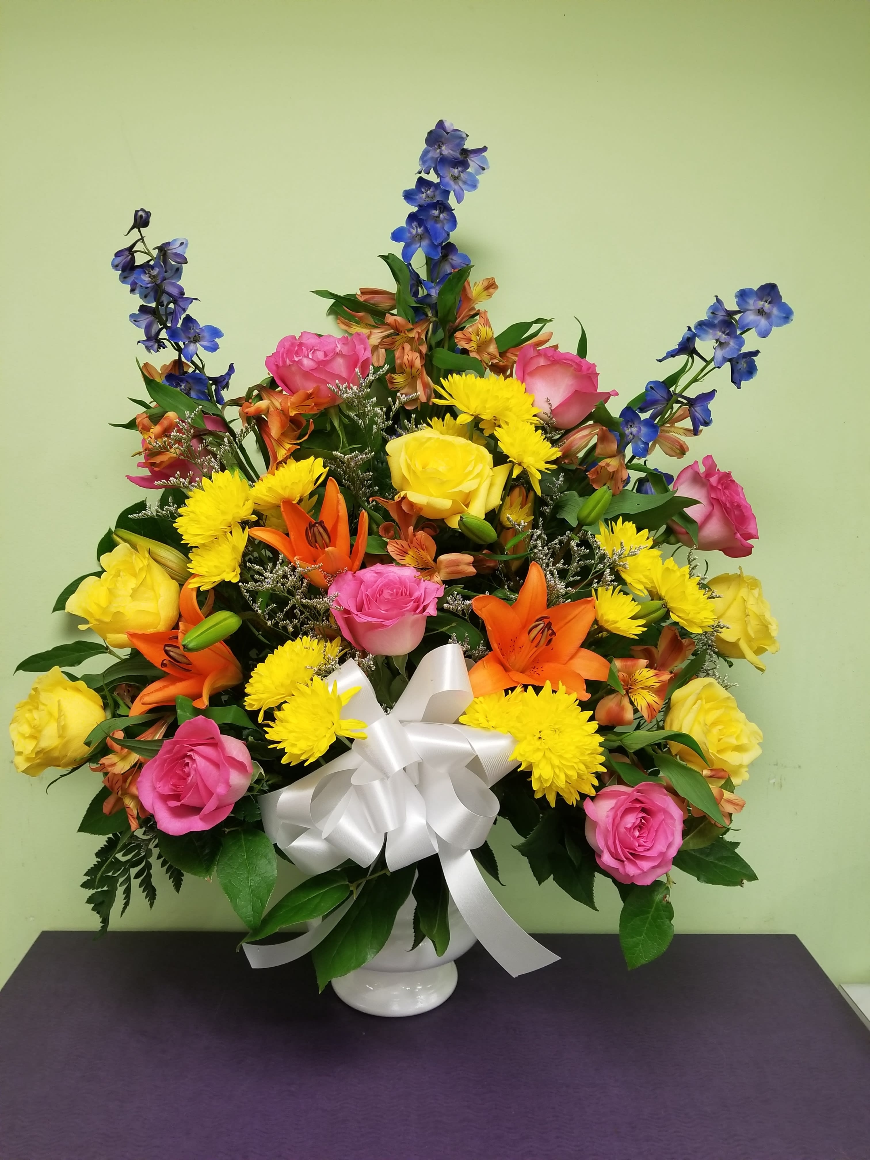 Colorful mixed flower arrangement in a white vase with a white bow