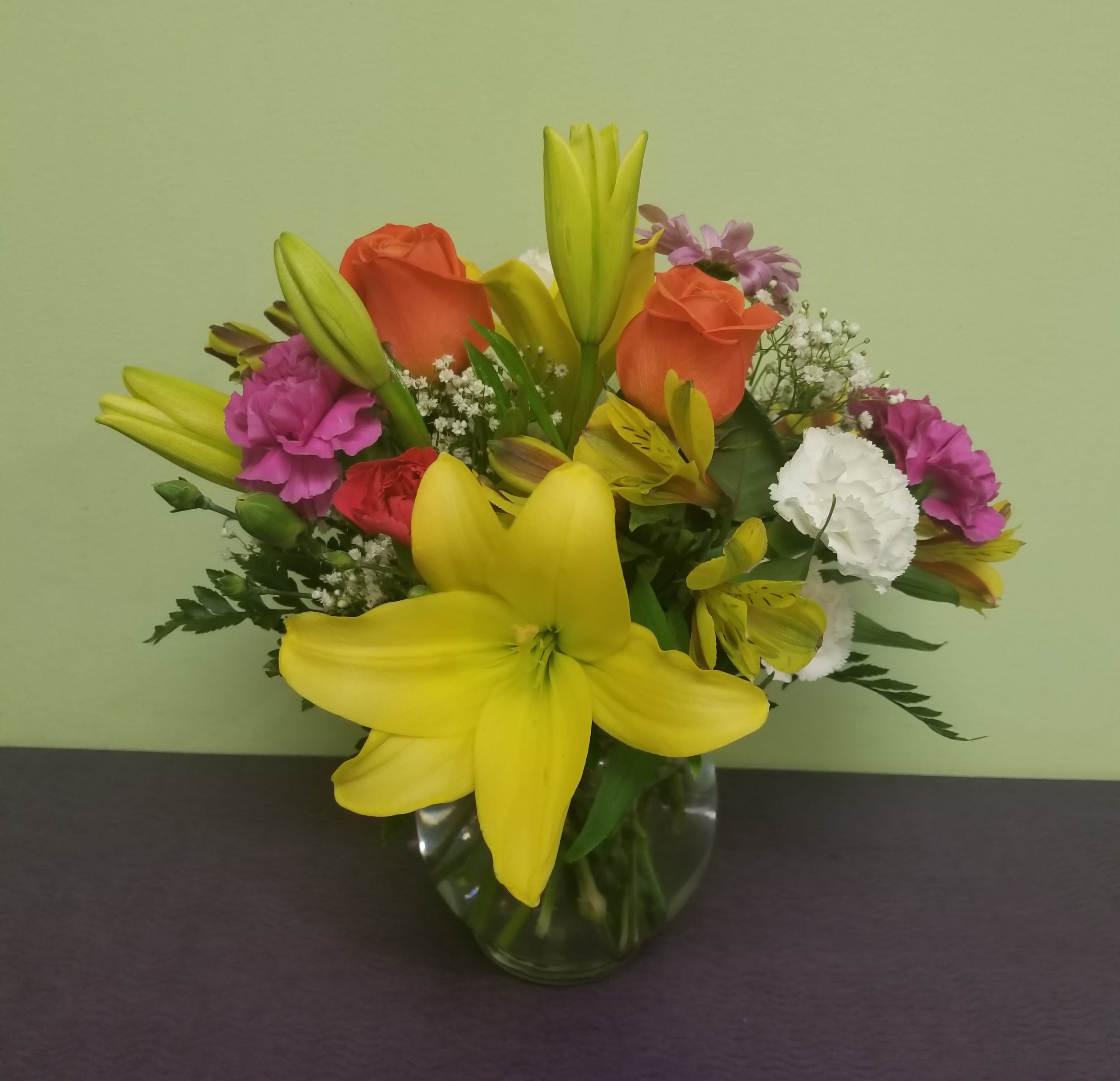 Mixed bouquet with yellow lilies, orange roses, and pink carnations in a glass vase