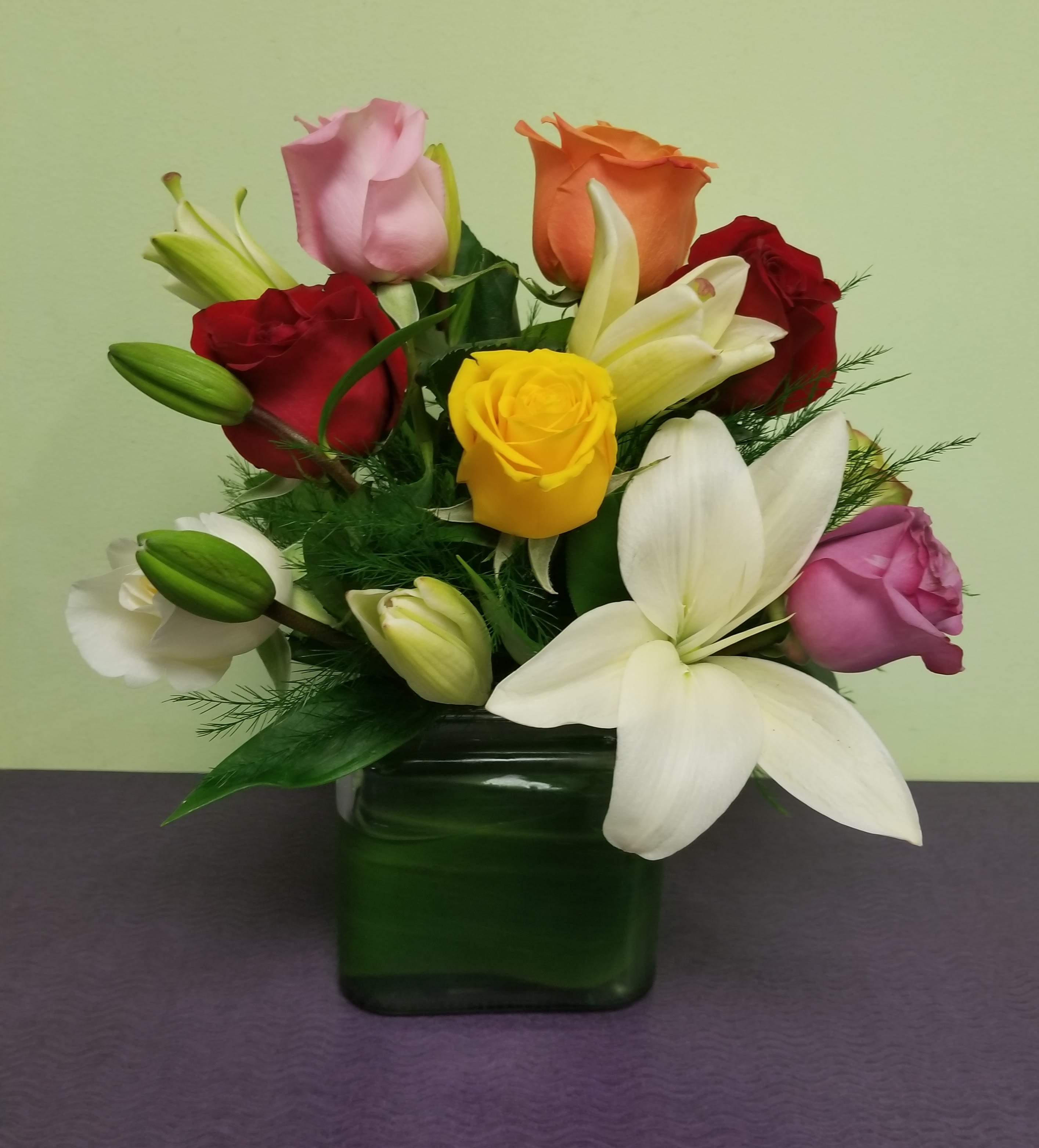 Mixed roses and lilies arranged in a green glass vase