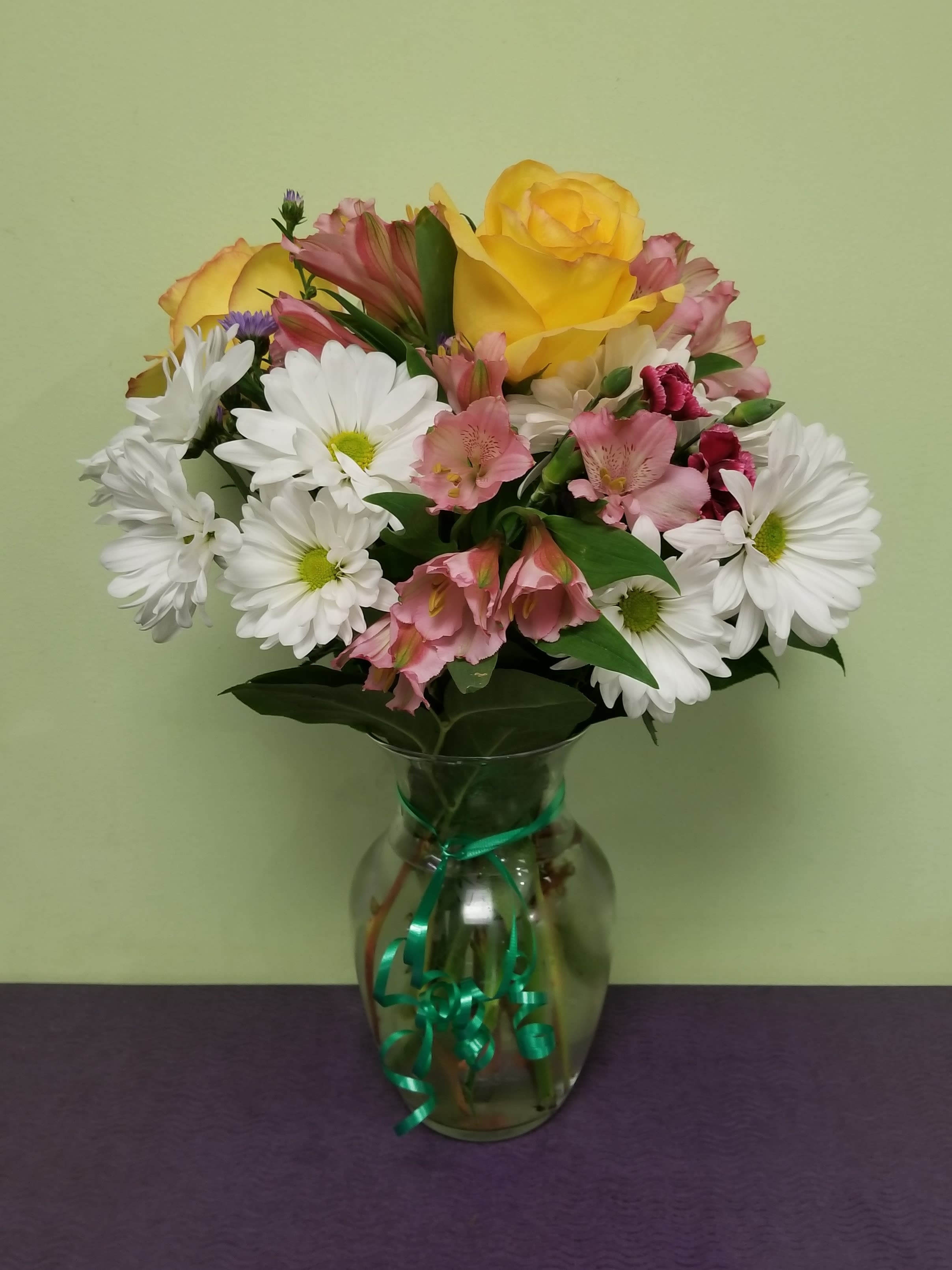 Bouquet of yellow roses, white daisies, and pink alstroemeria in a glass vase