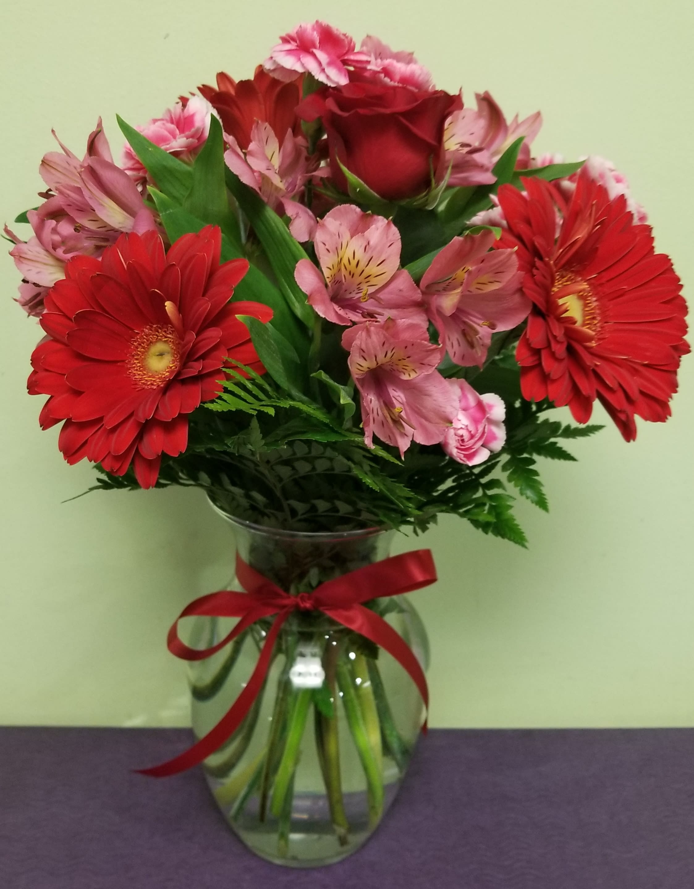 Red gerbera daisies and pink roses in a glass vase with a red ribbon