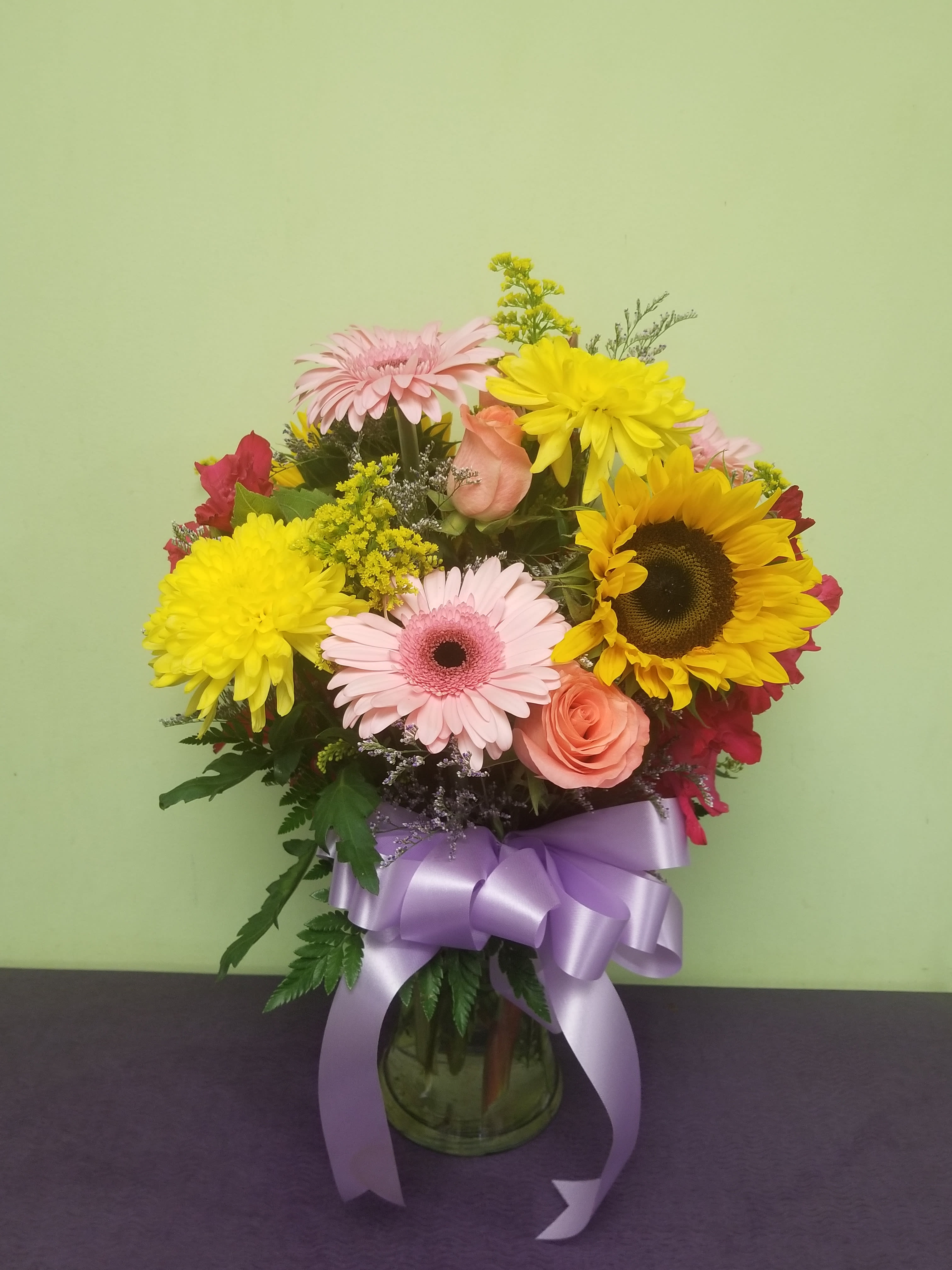 Mixed bouquet with sunflowers, pink gerberas, and roses in a glass vase