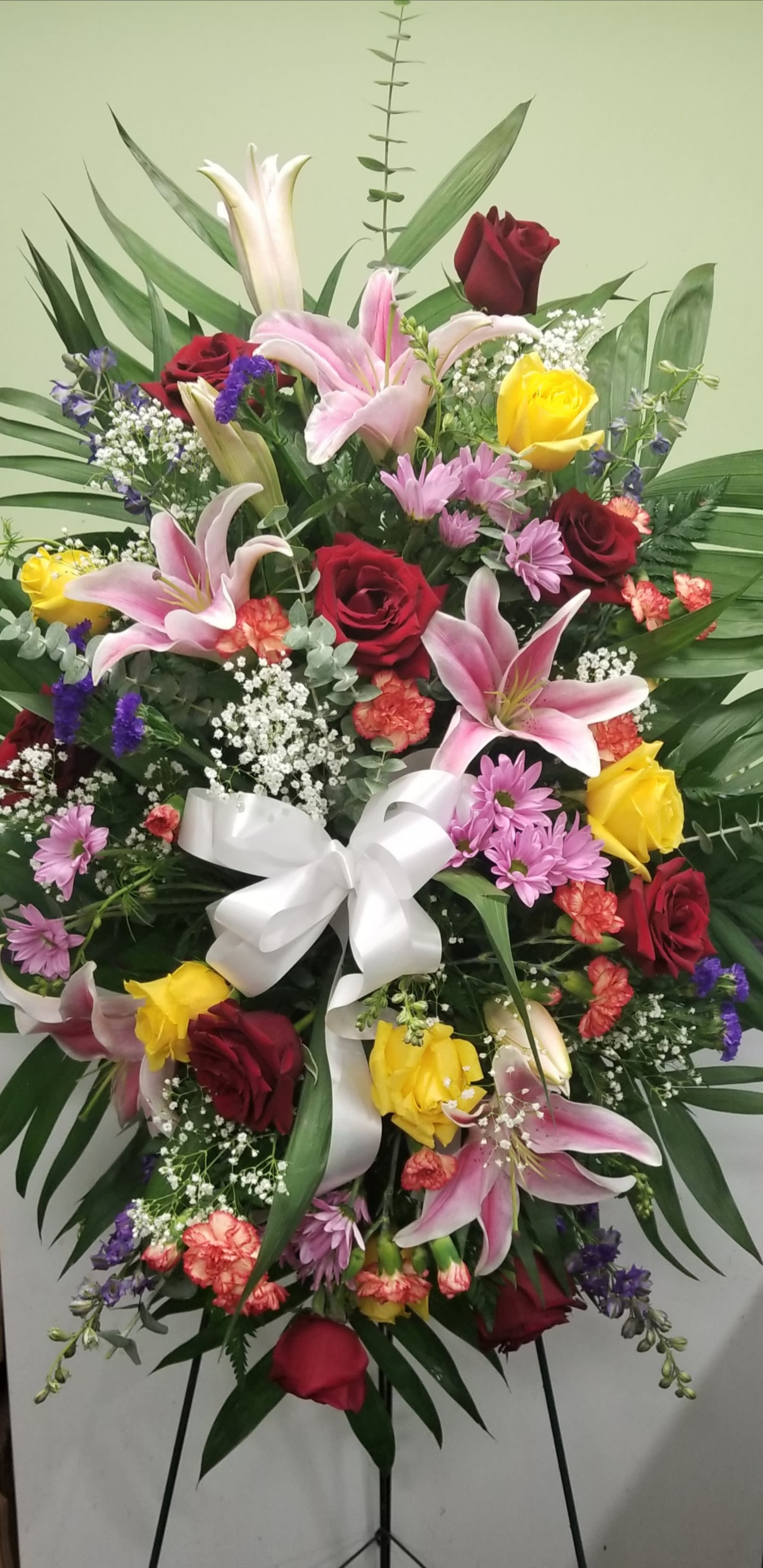 Standing floral spray with roses, lilies, and a white ribbon bow