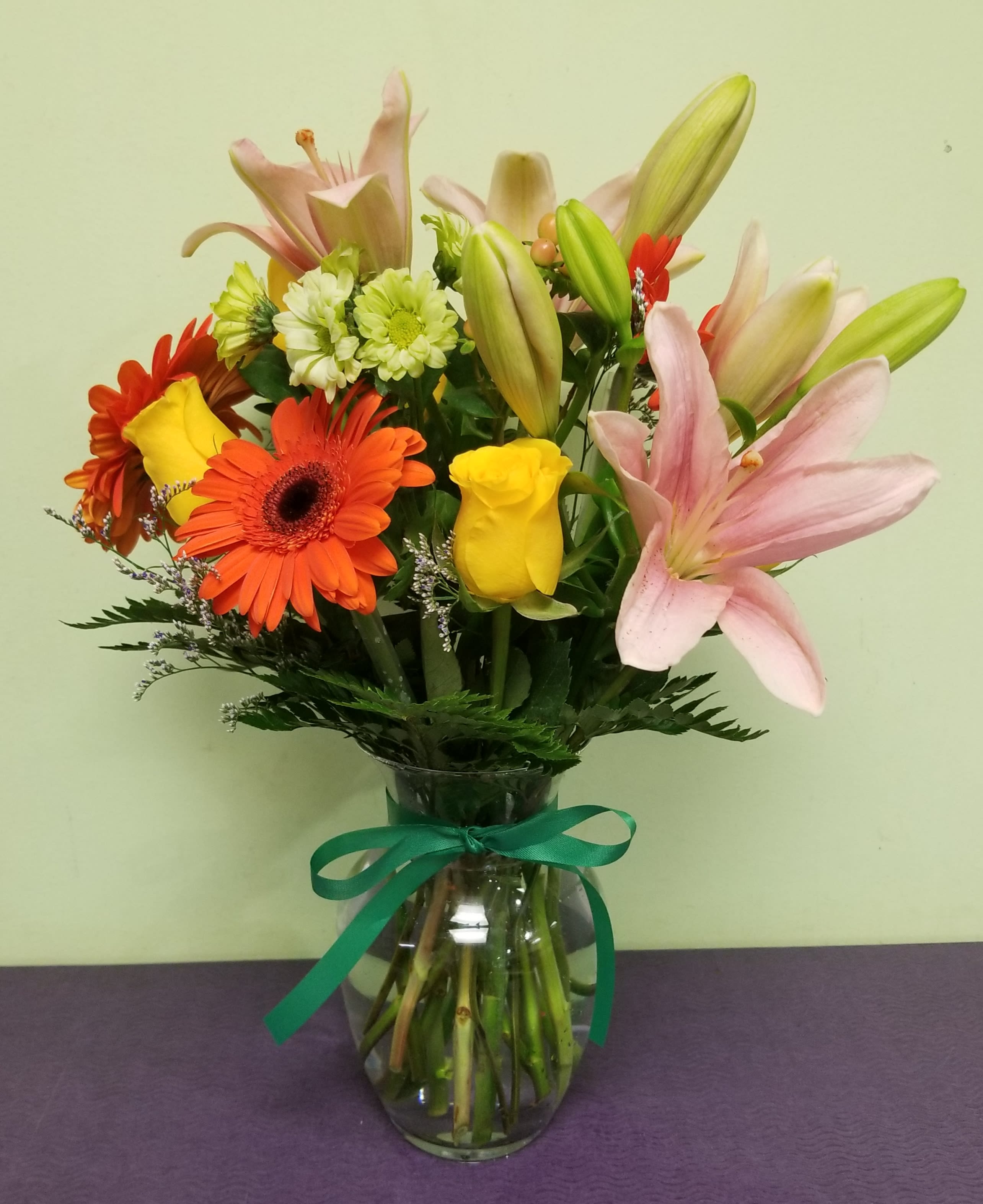 Mixed bouquet of lilies, roses, and gerbera daisies in a glass vase with ribbon