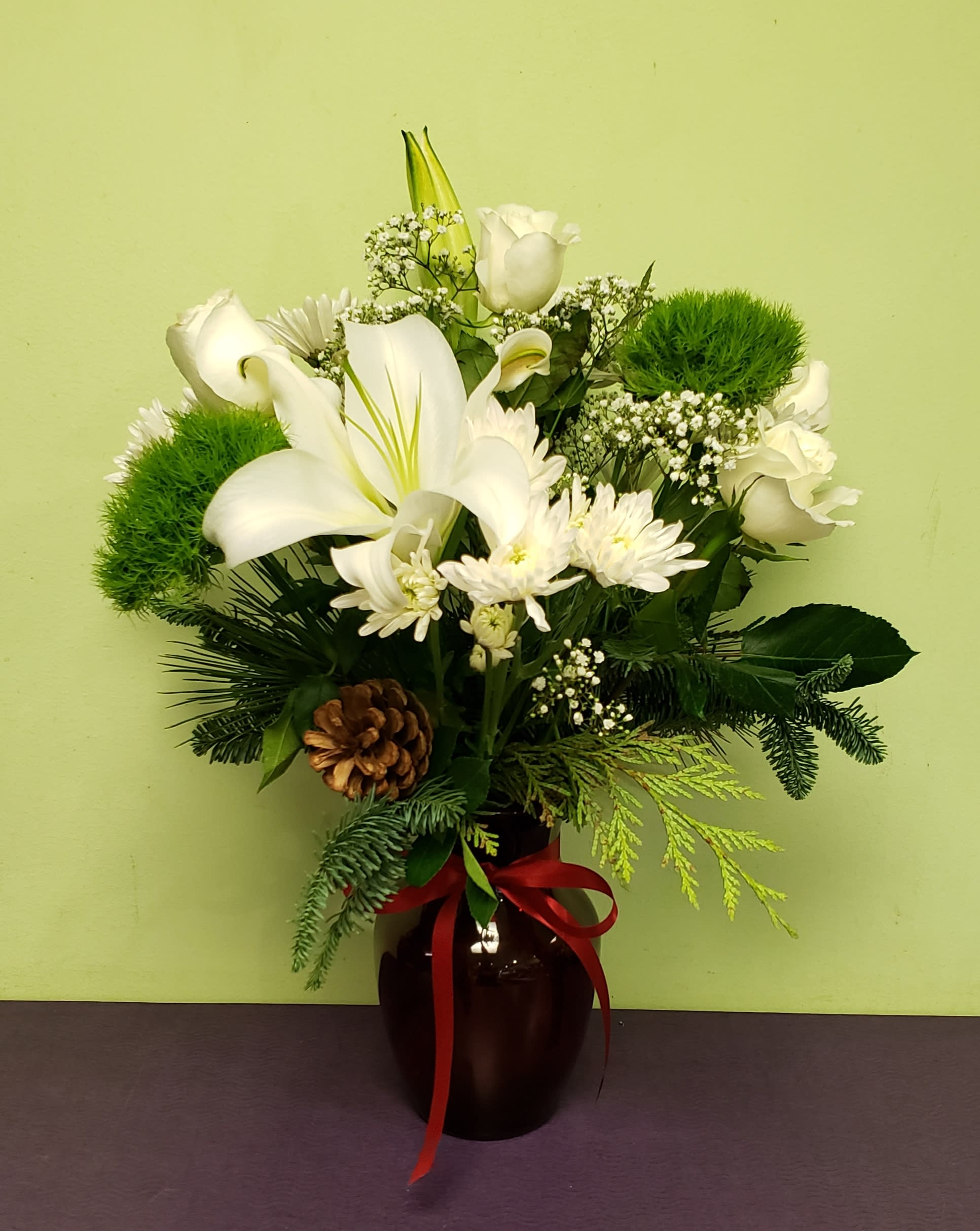 White lilies and roses arranged in a dark vase with a red ribbon