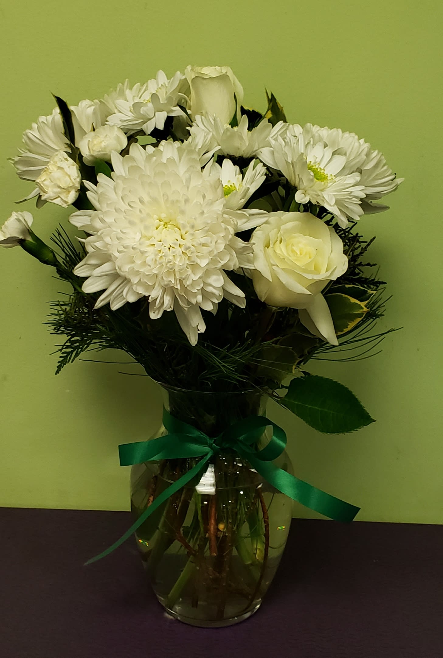 White flowers arranged in a glass vase with a green ribbon