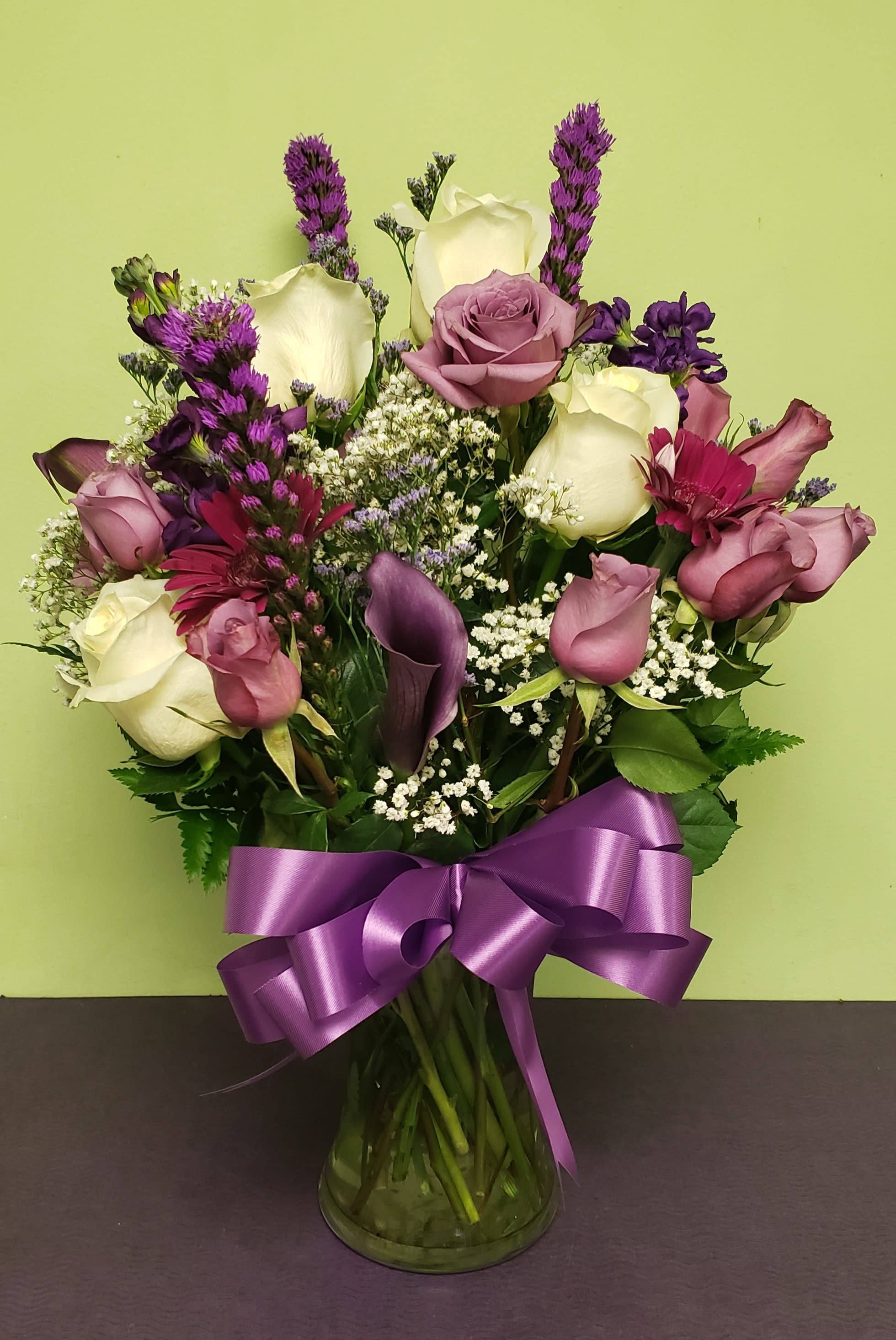 Mixed bouquet of roses, calla lilies, and purple flowers in a glass vase with a ribbon