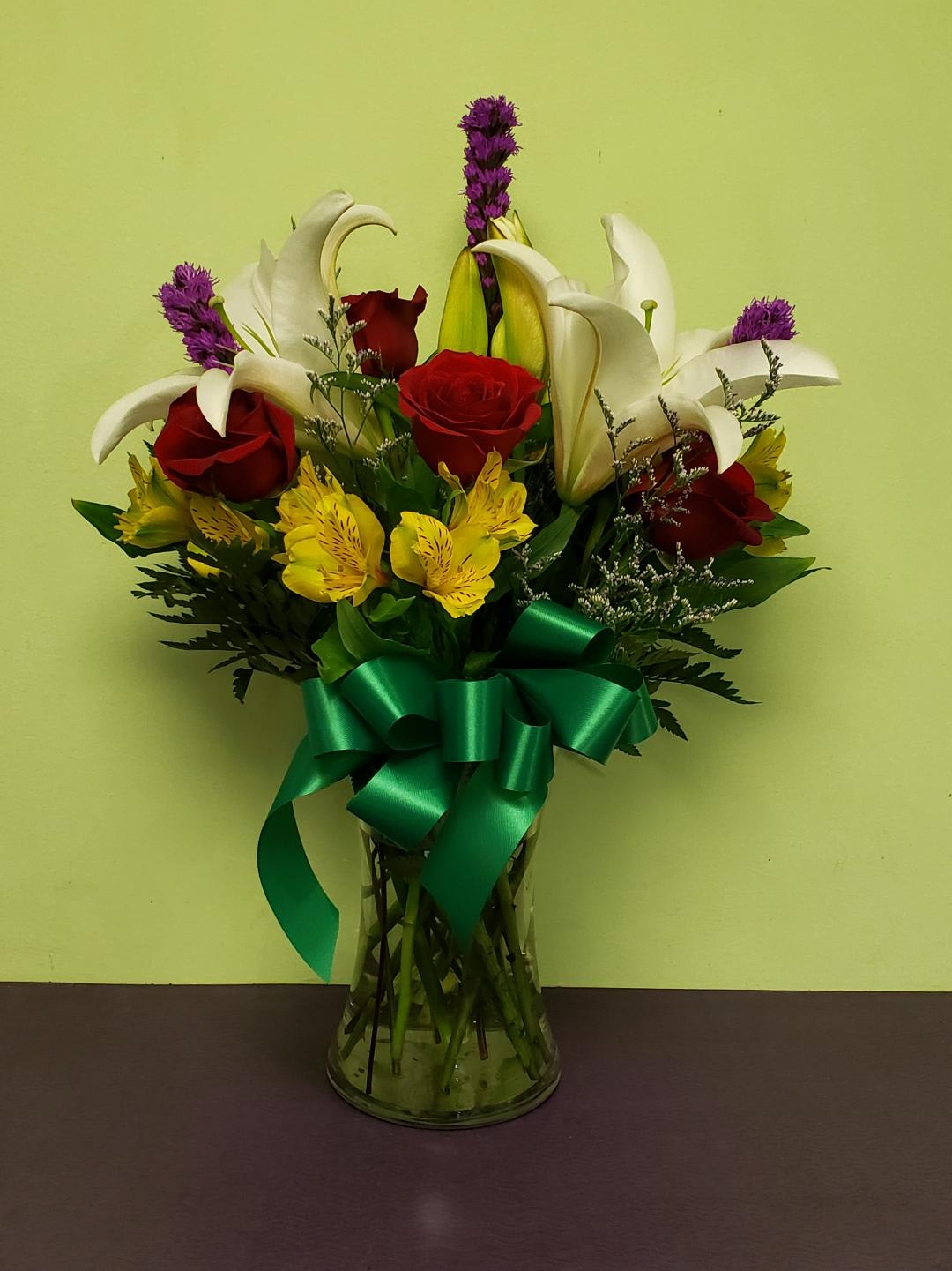 Bouquet of red roses, white lilies, and yellow alstroemeria in a glass vase