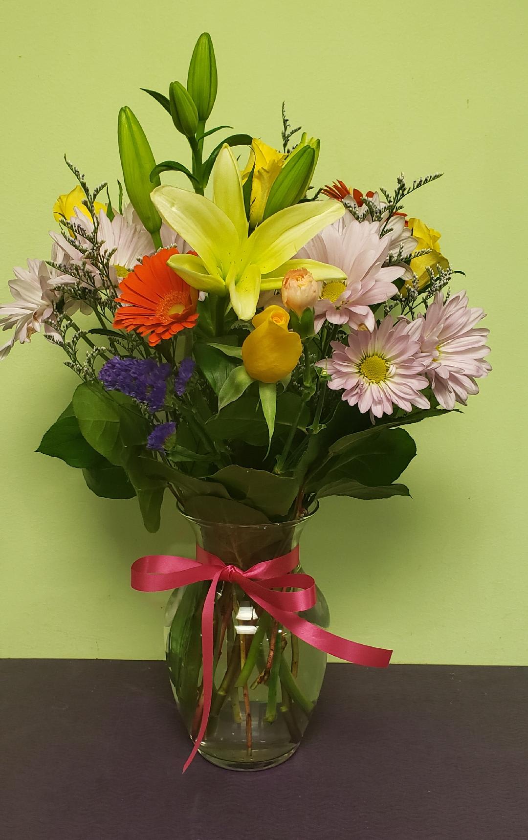 Mixed bouquet with a yellow lily in a glass vase tied with a pink ribbon