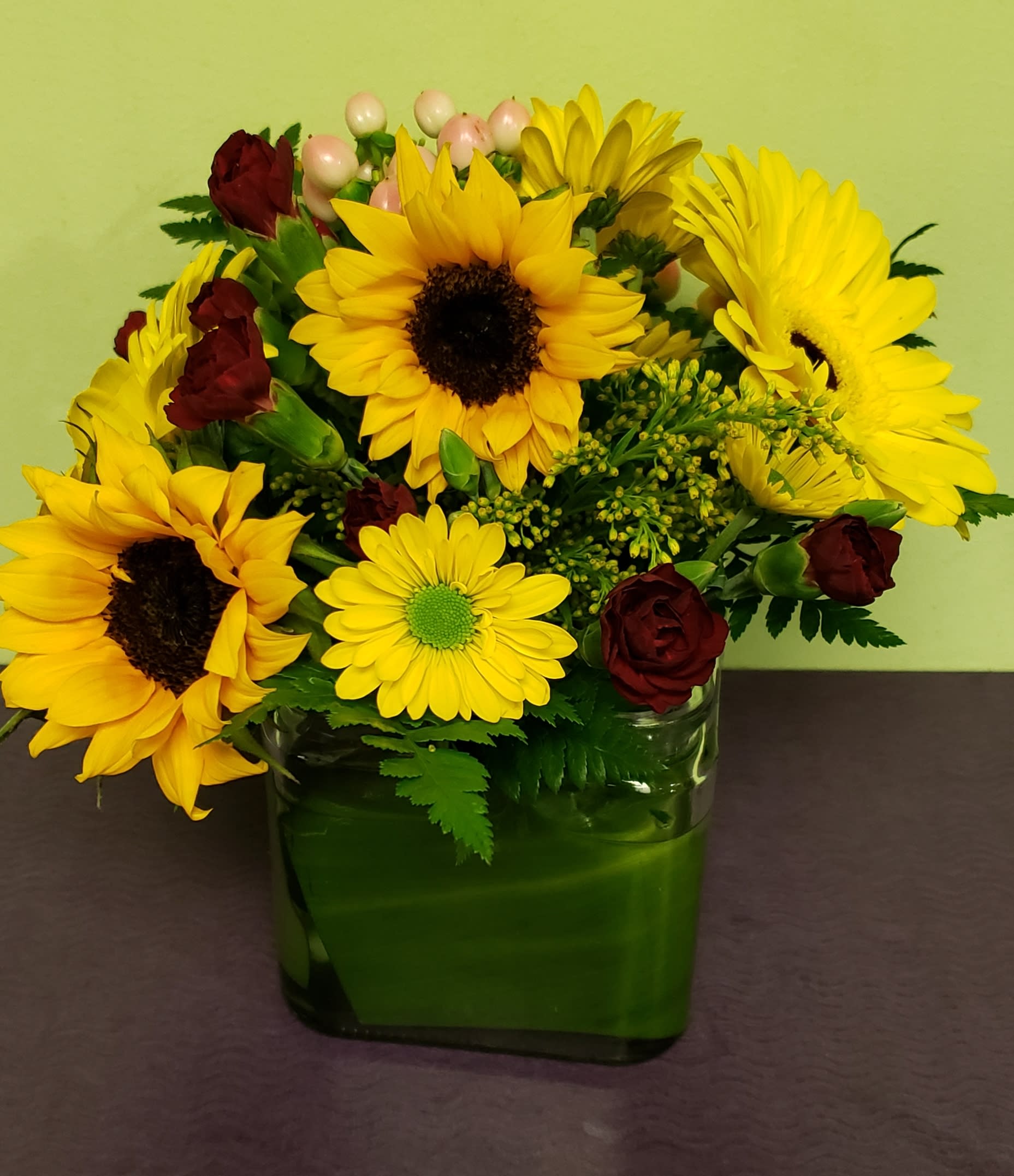 Sunflower and burgundy rose arrangement in a green glass vase