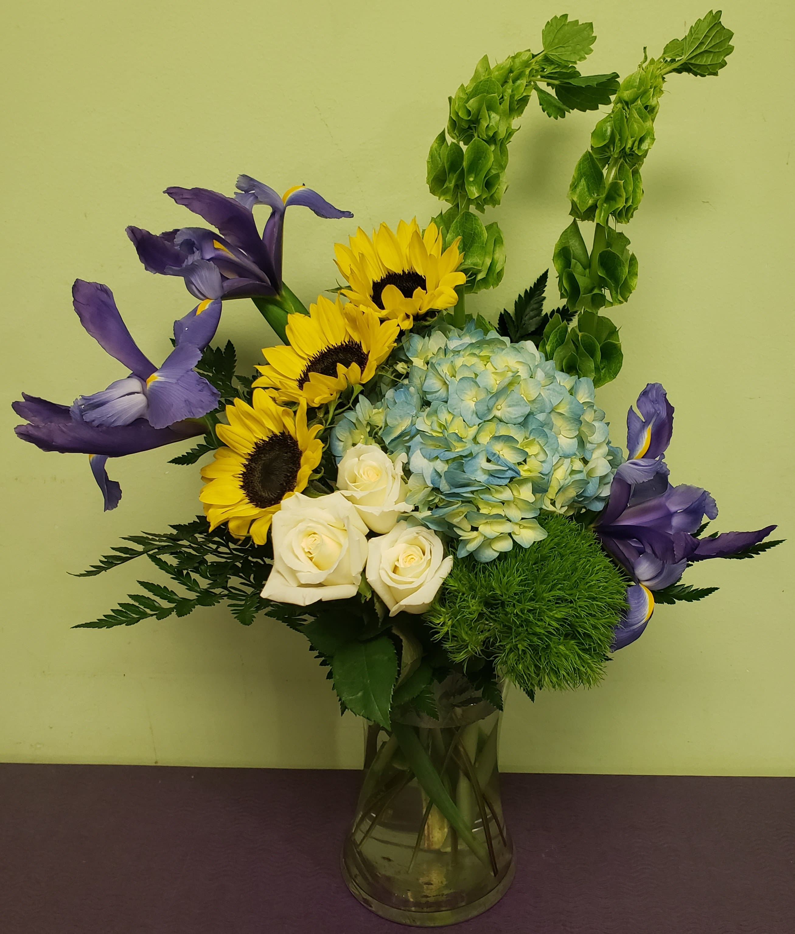 Bouquet of sunflowers, white roses, blue hydrangea, and purple irises in a glass vase
