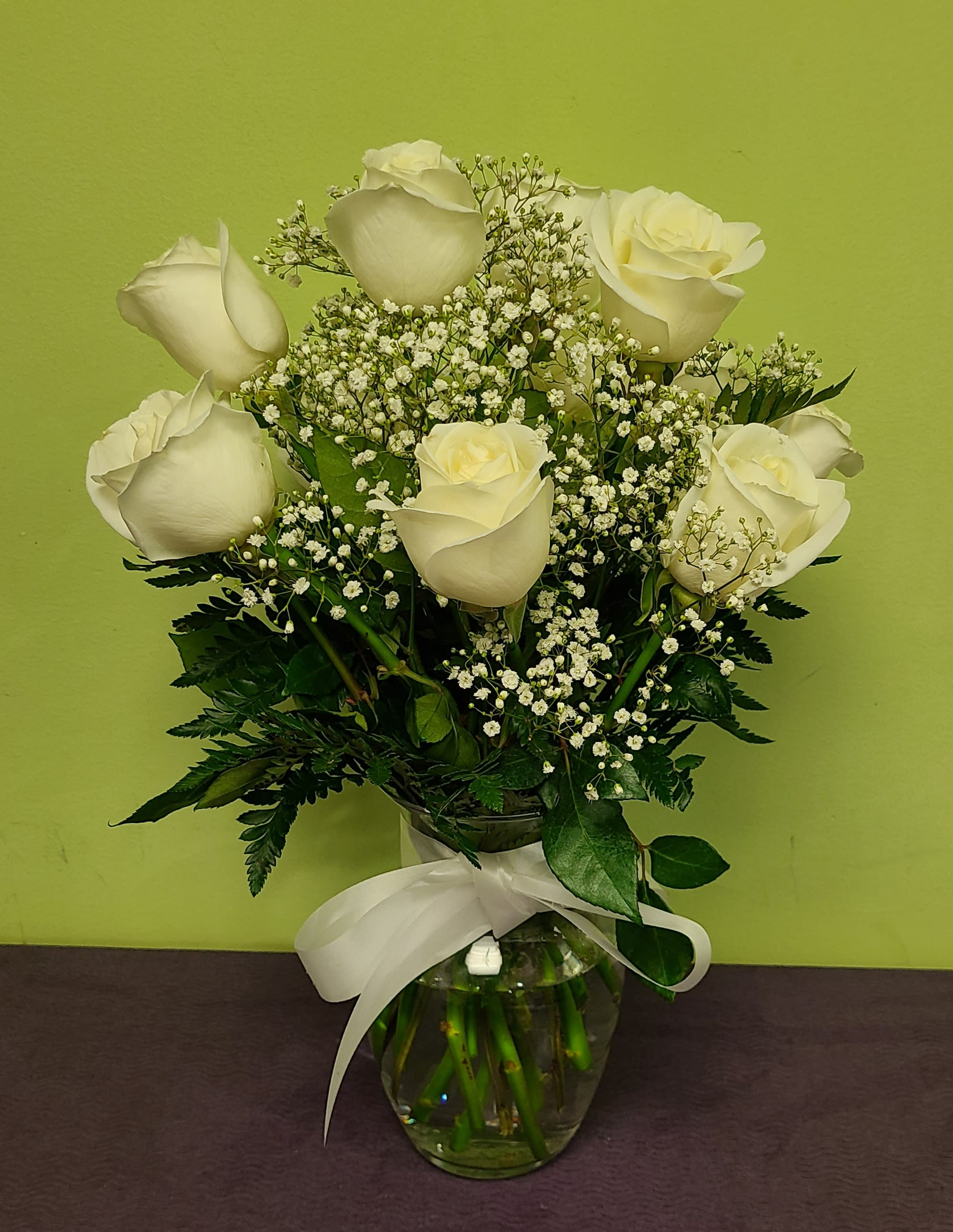 White roses and baby's breath in a glass vase with a white ribbon