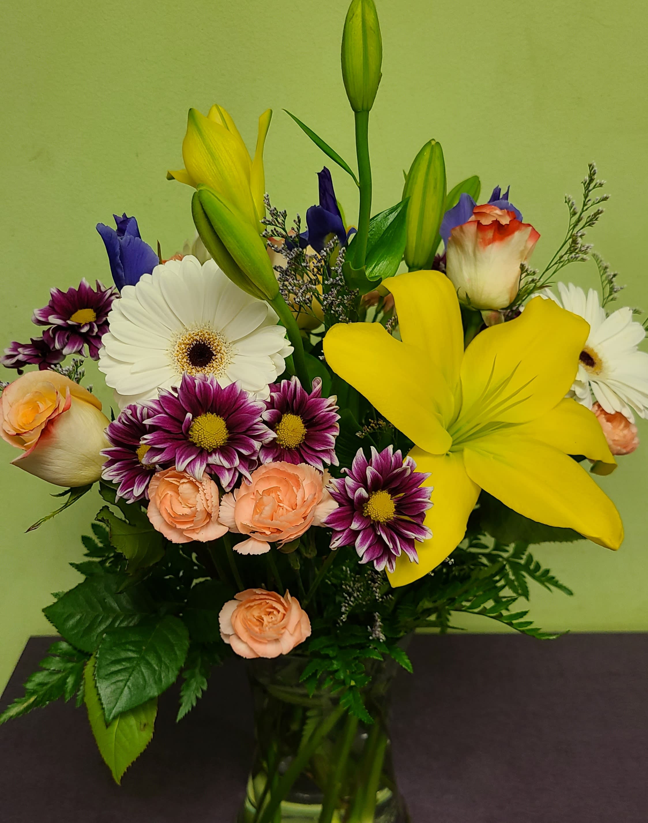 Mixed bouquet with yellow lilies, white gerberas, and peach roses in a glass vase