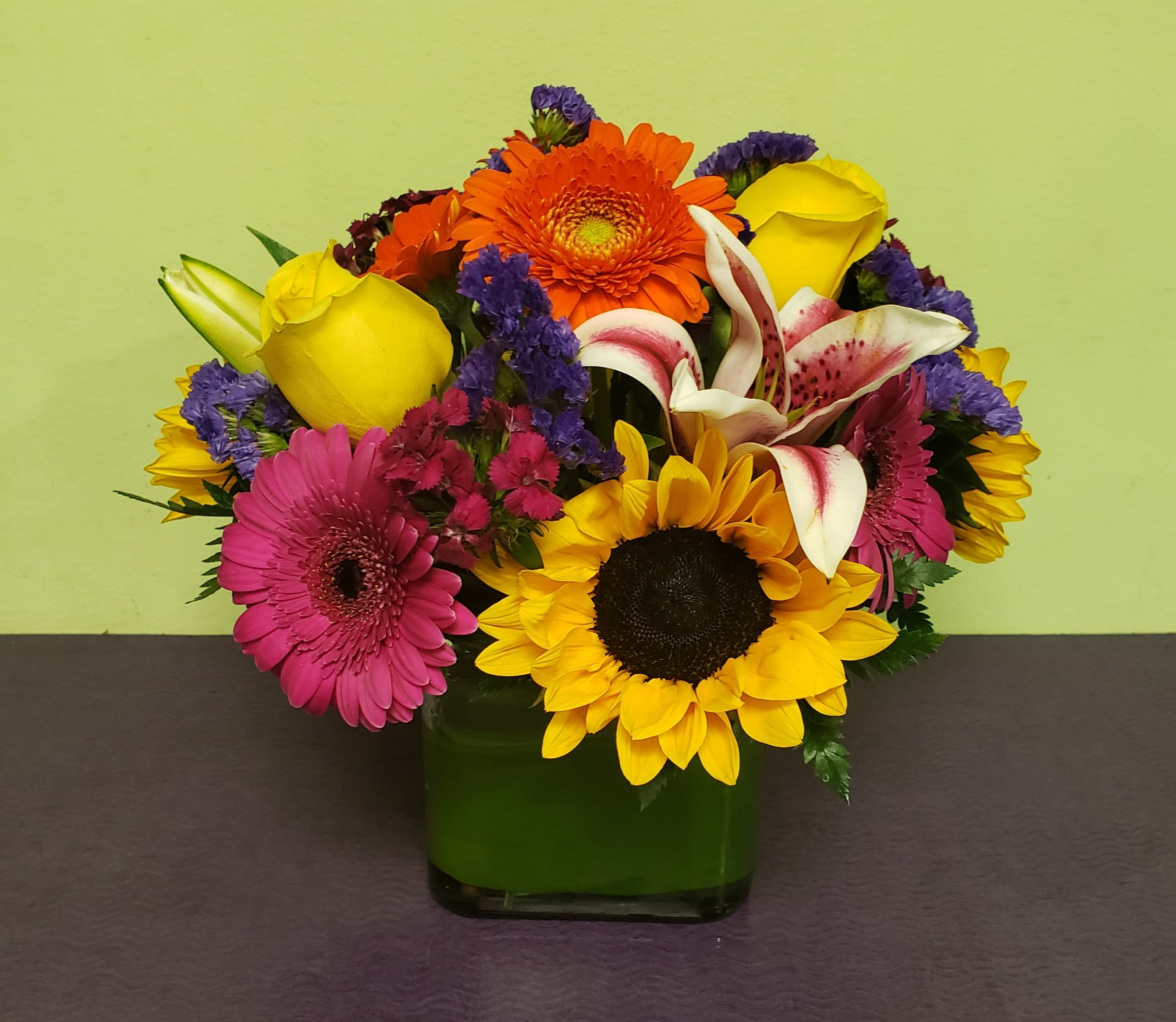 Colorful mixed bouquet in a green glass vase with sunflowers and roses