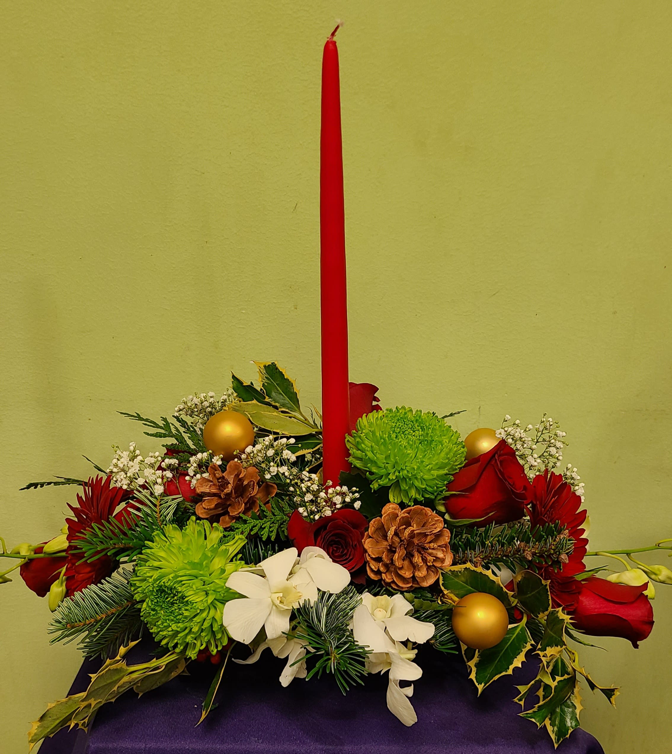 Holiday centerpiece with red candle, red roses, green mums, and white orchids