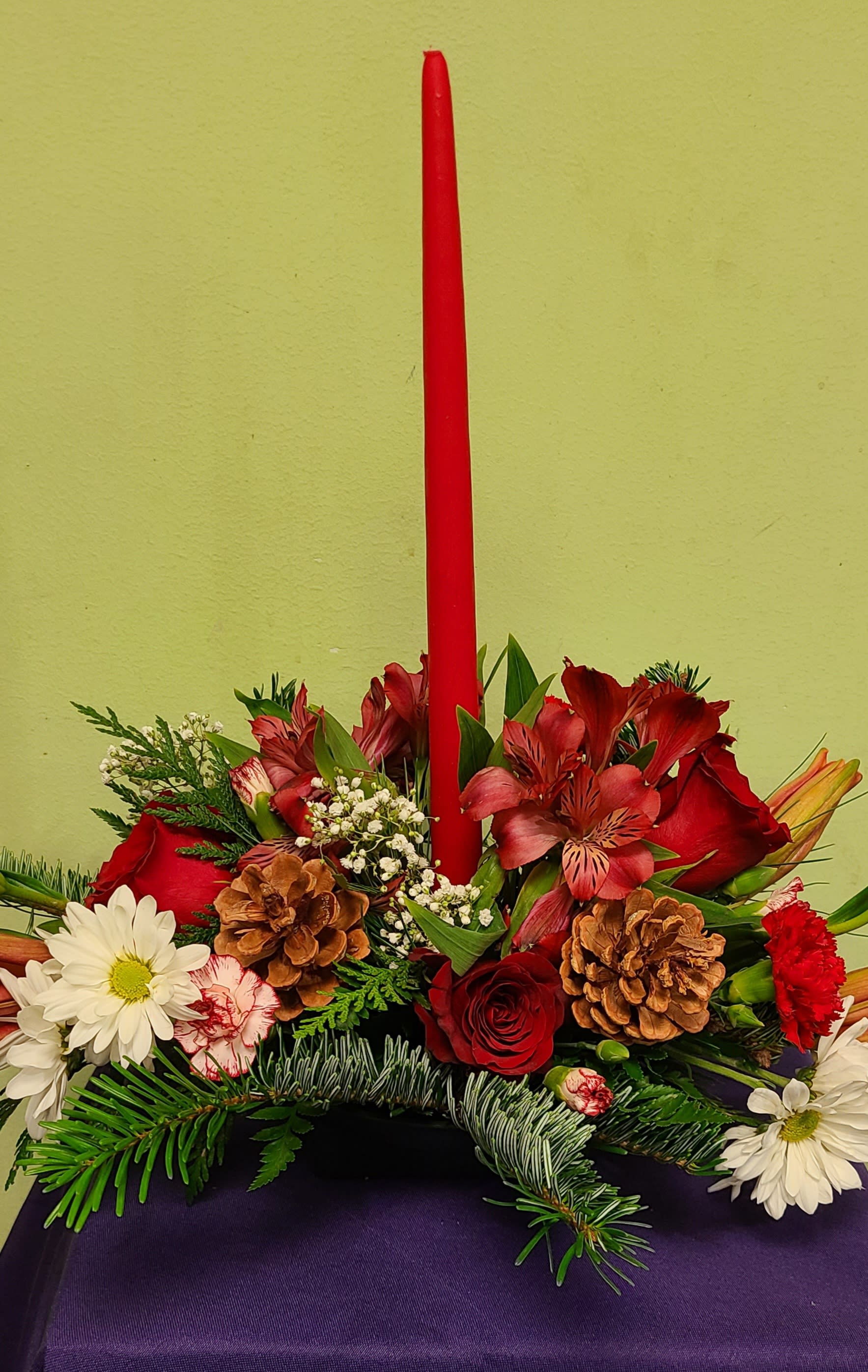 Red candle in a floral arrangement with roses, daisies, and pinecones