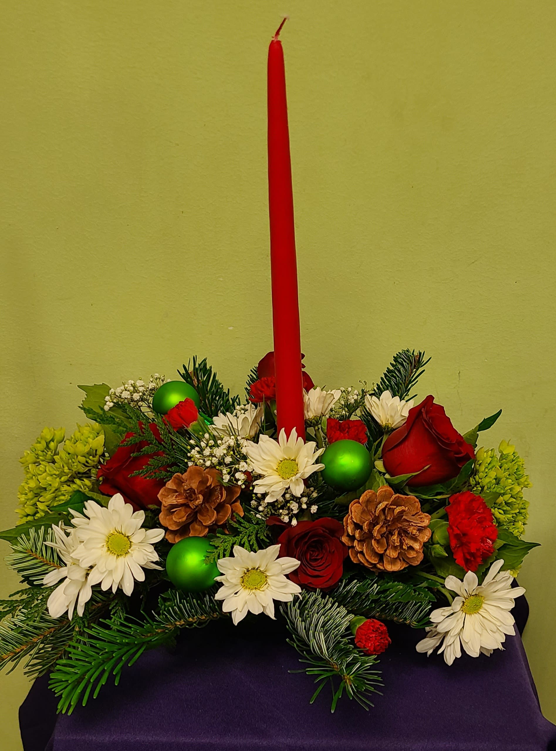 Christmas centerpiece with red candle, roses, white daisies, and pinecones