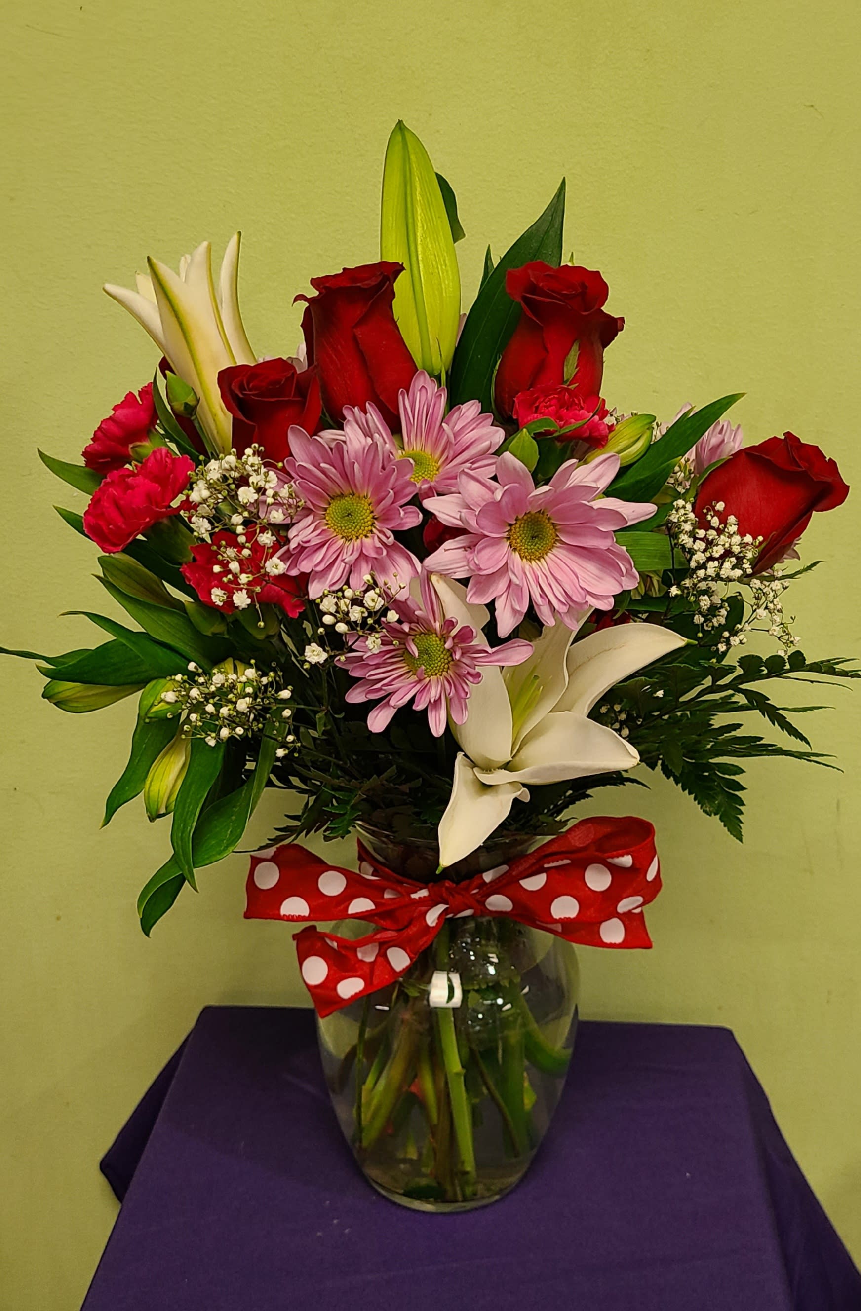 Bouquet of red roses, pink daisies, and white lilies in a glass vase