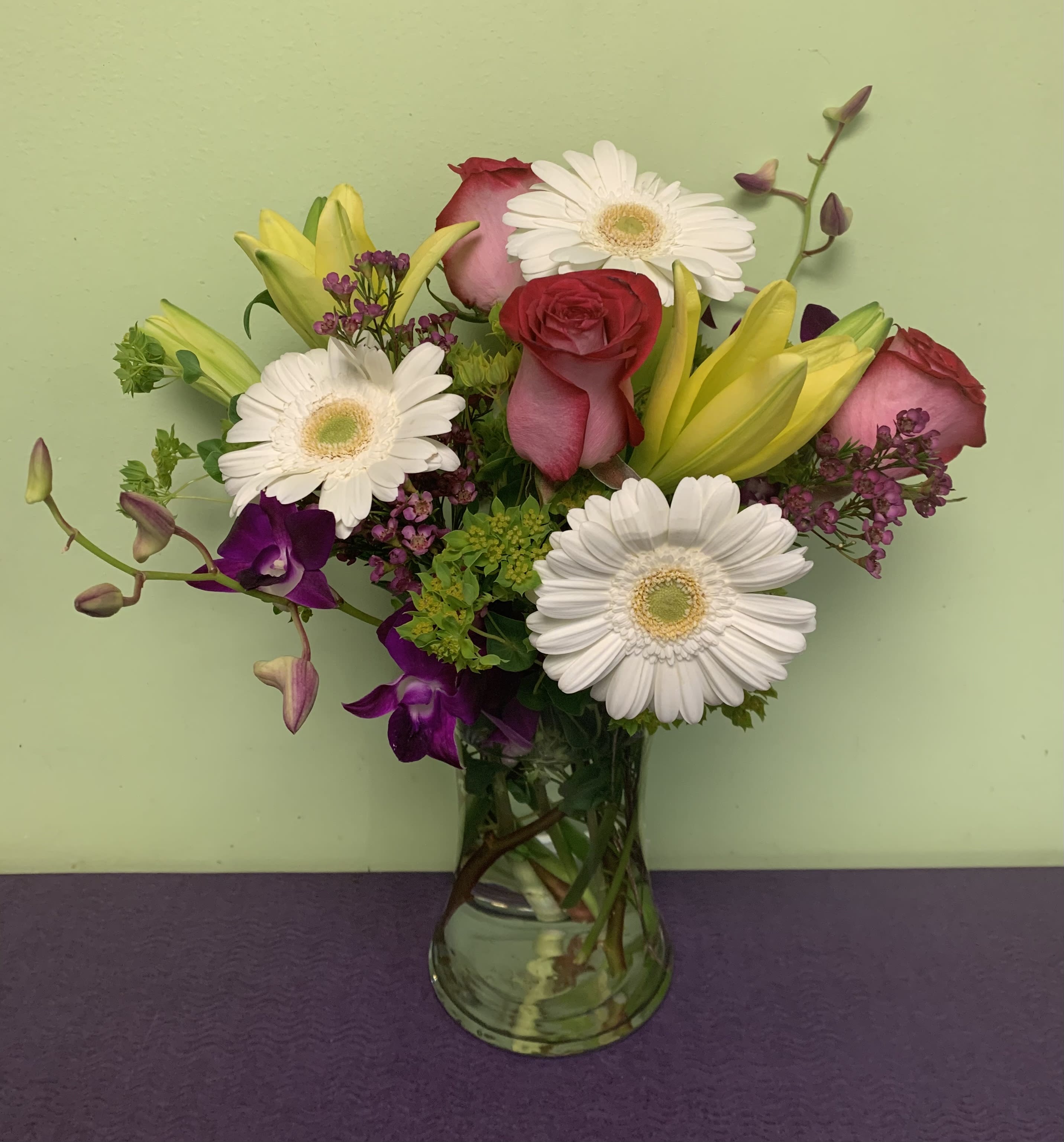 Mixed bouquet of roses, gerbera daisies, lilies, and orchids in a glass vase
