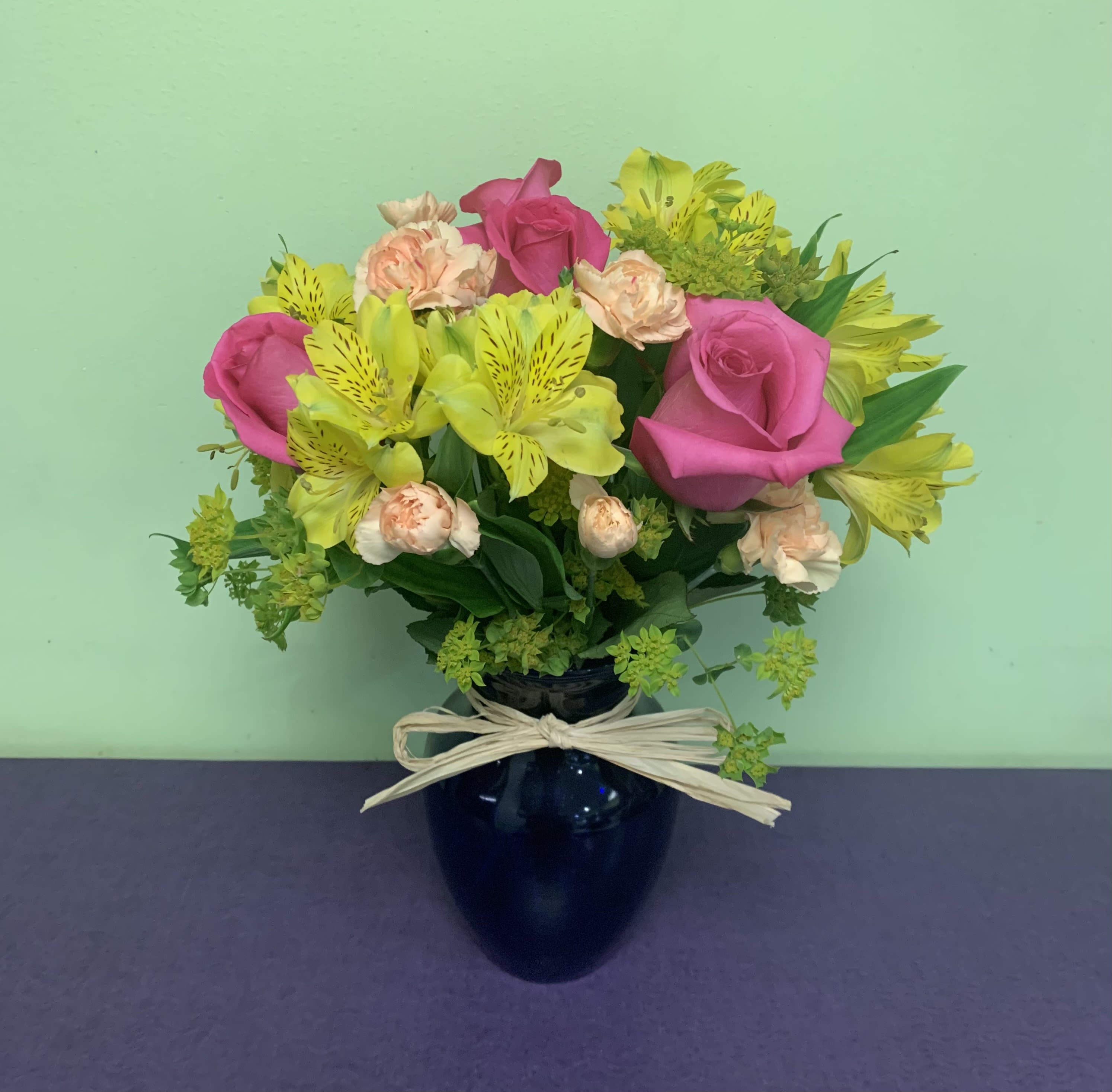 Pink roses and yellow alstroemeria in a dark vase with a bow