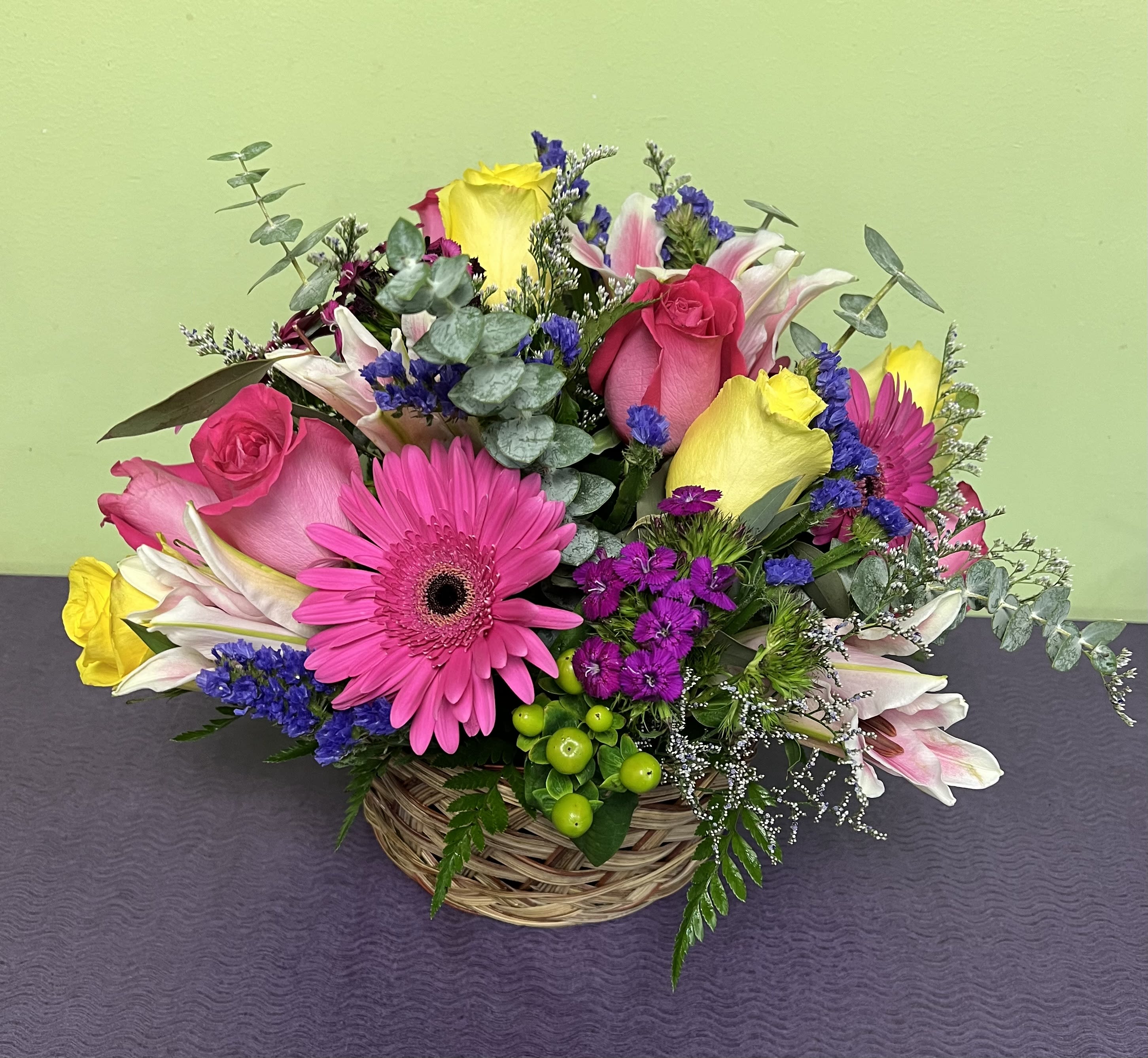 Basket arrangement with pink roses, gerbera daisies, lilies, and purple filler flowers