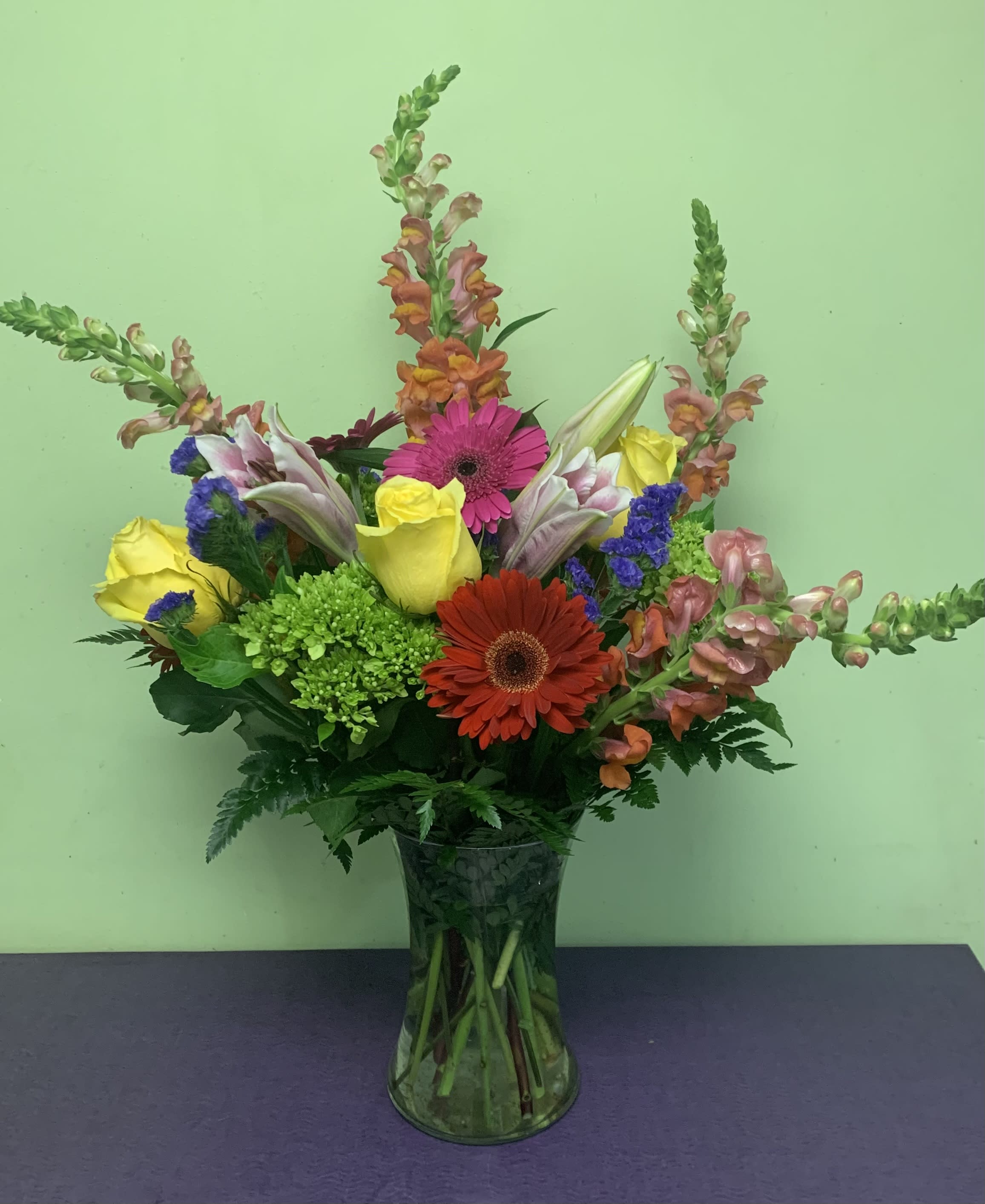 Mixed bouquet with roses, gerbera daisies, lilies, and snapdragons in a glass vase