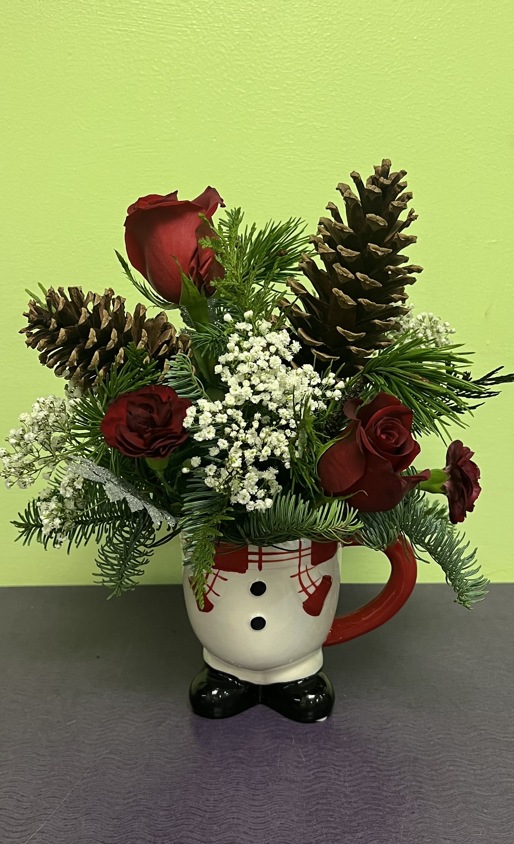 Red roses and pinecones arranged in a snowman mug