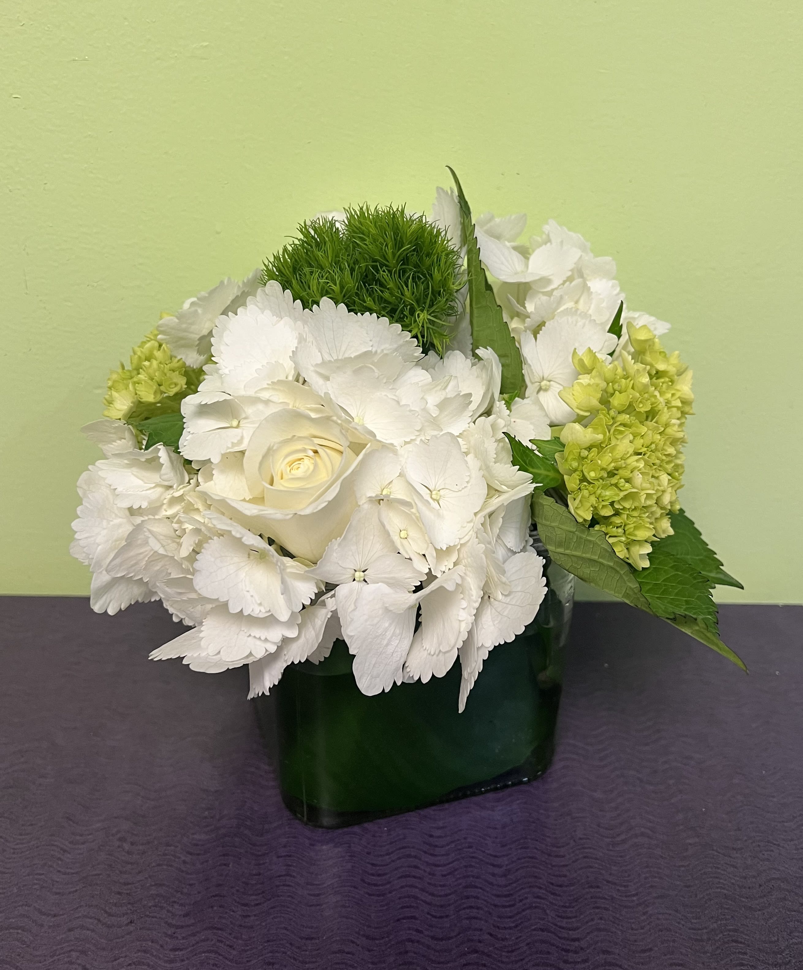 White hydrangeas and a cream rose in a dark green vase