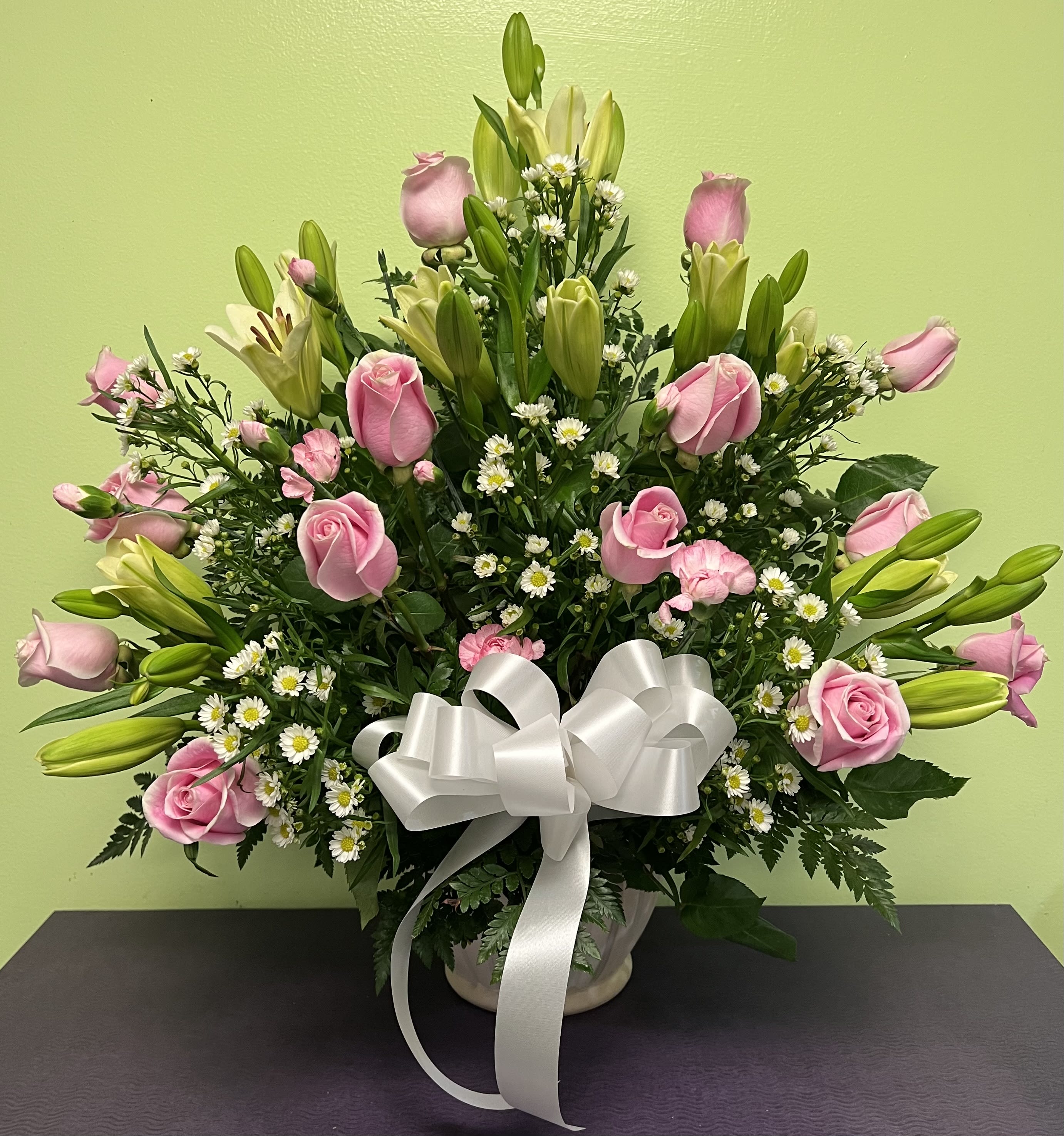 Pink roses and lilies arranged in a vase with a white ribbon bow