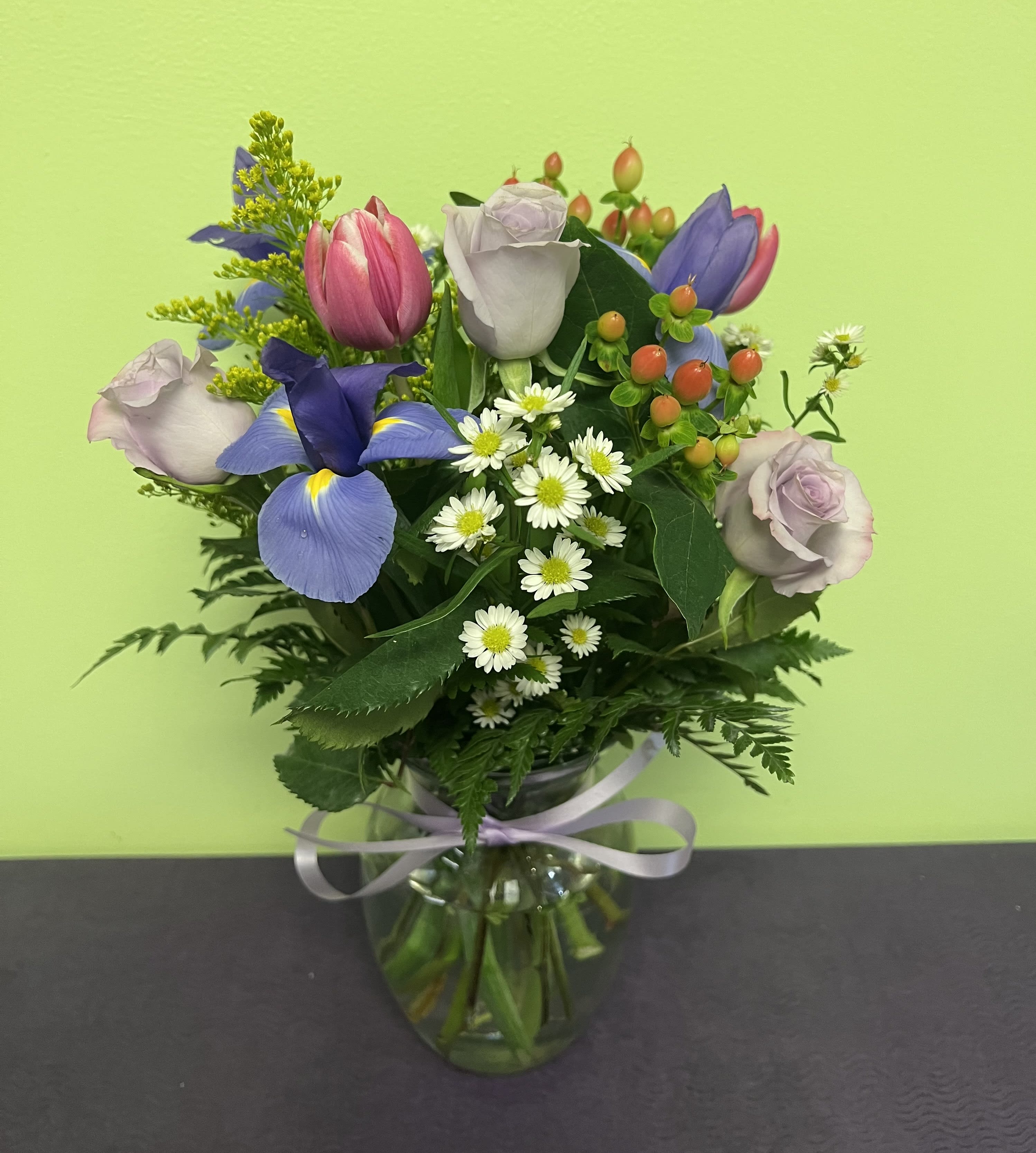 Mixed bouquet of roses, tulips, and daisies in a glass vase