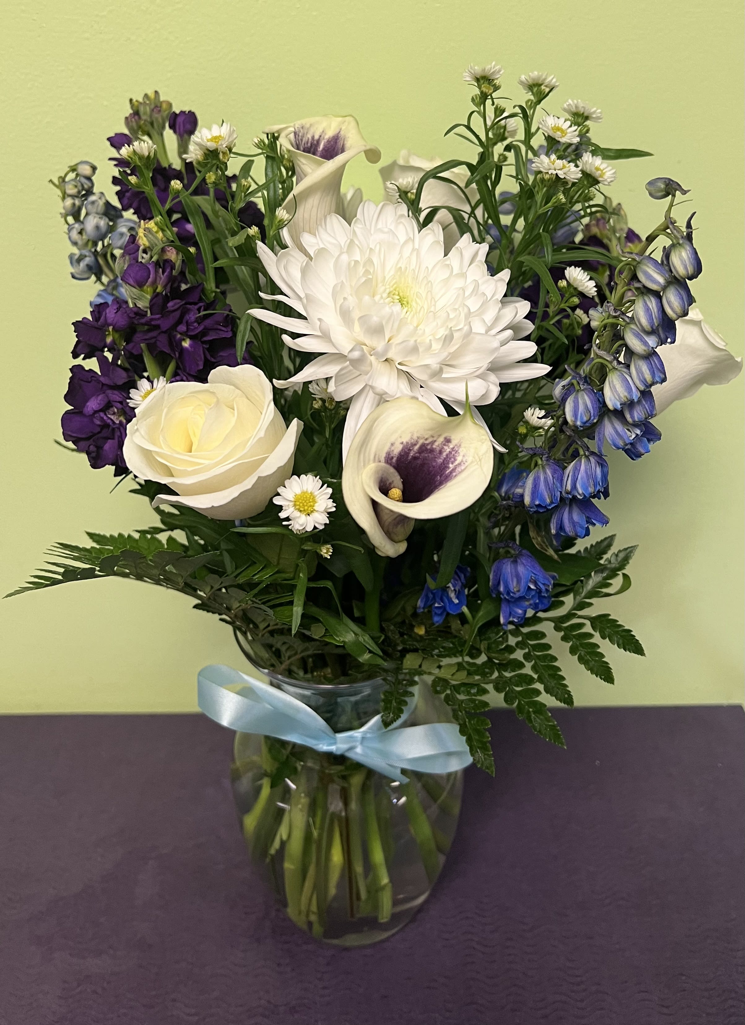 Bouquet of white, purple, and blue flowers in a glass vase with a blue ribbon