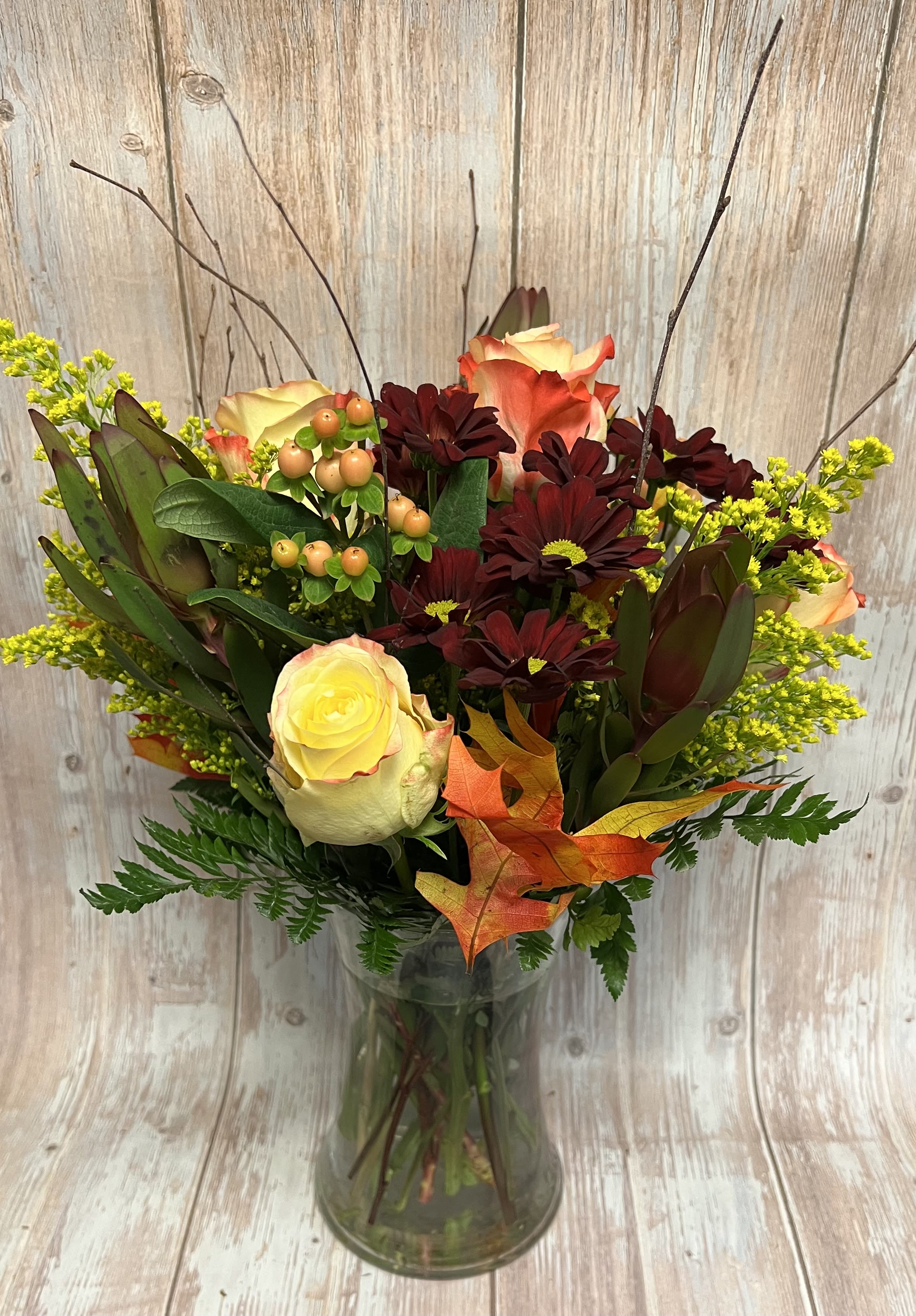 Bouquet of cream and orange roses with dark burgundy daisies in a glass vase