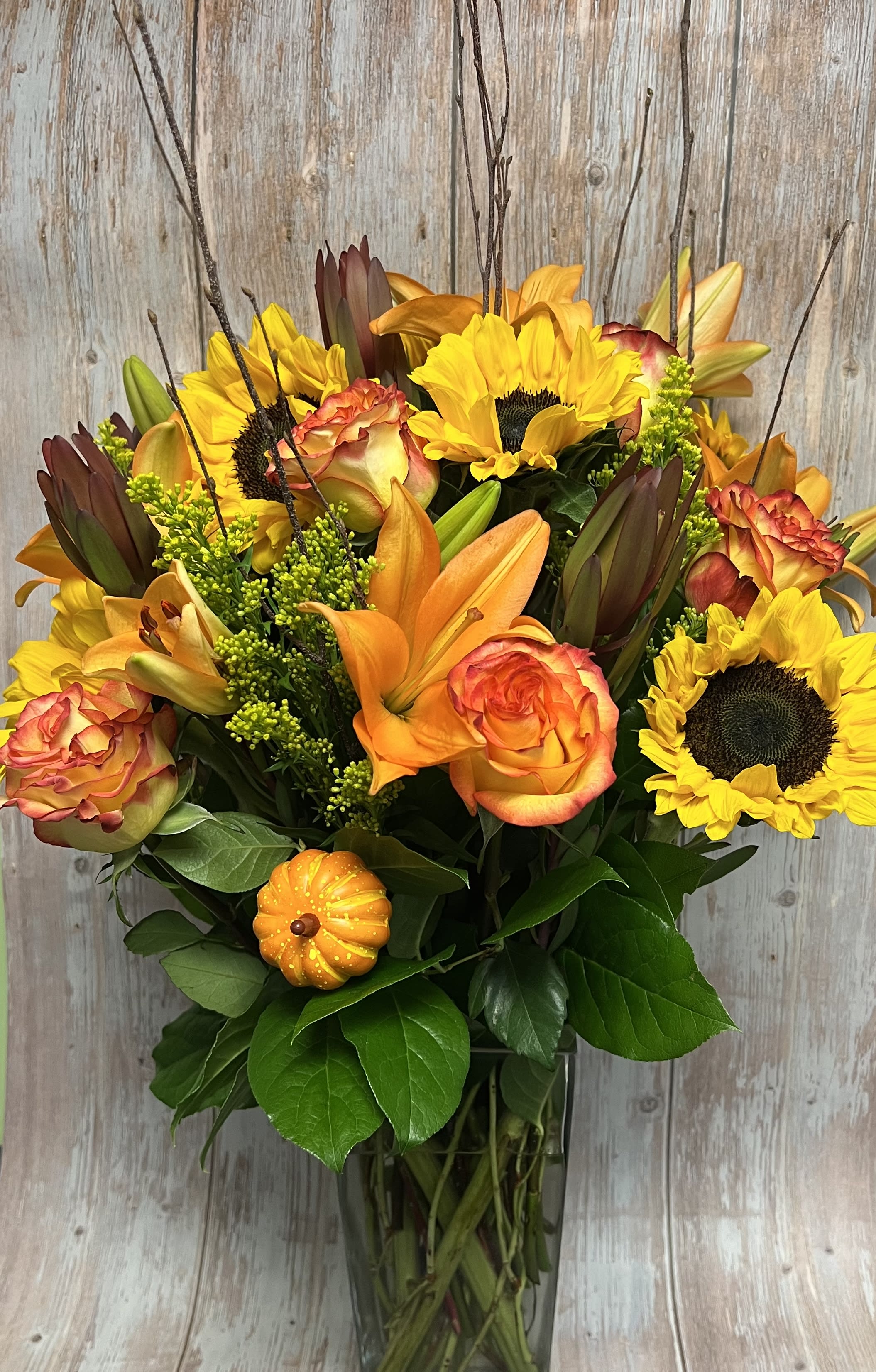 Bouquet of sunflowers, orange roses, and lilies in a glass vase