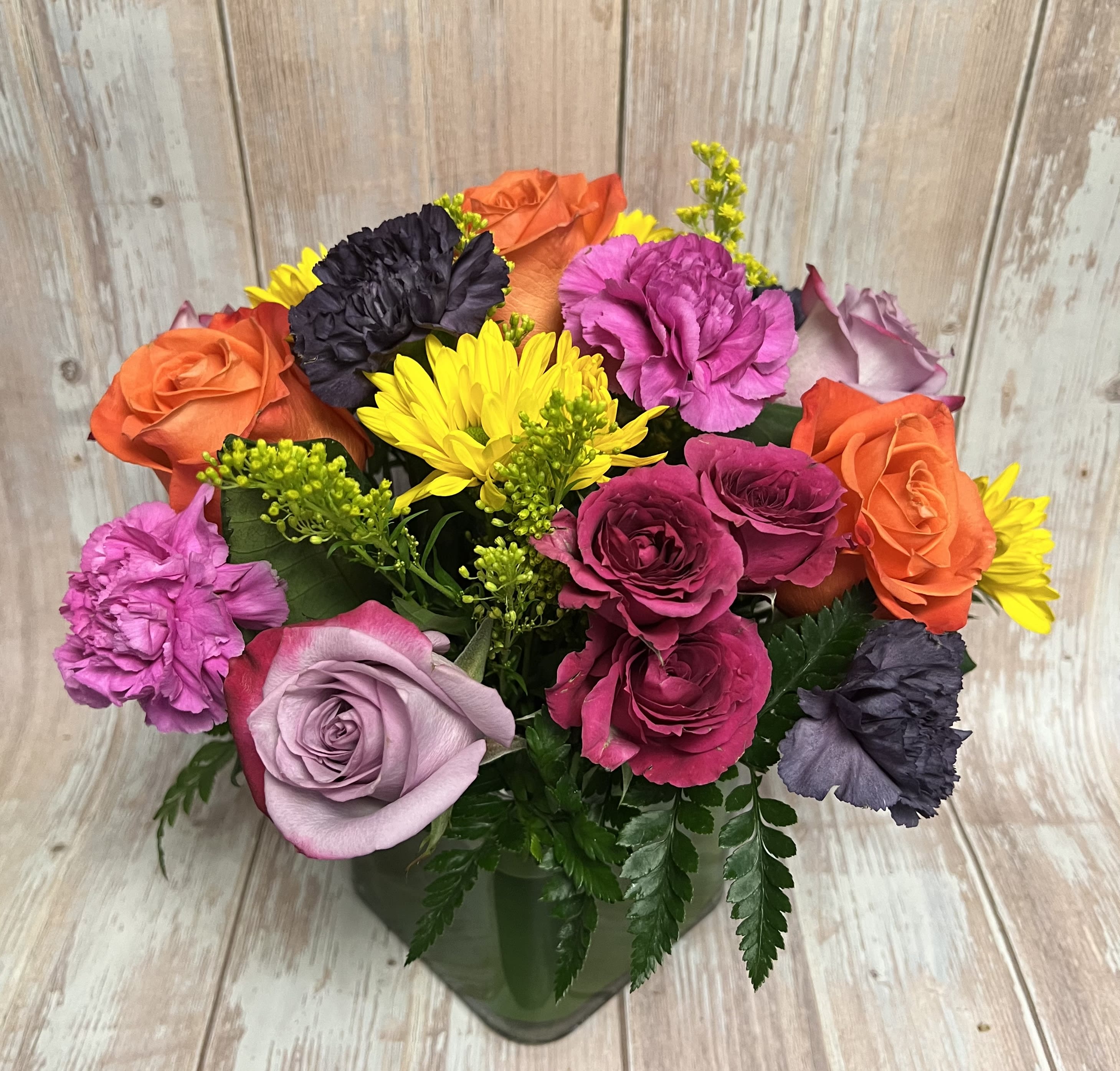 Colorful bouquet of roses, carnations, and yellow daisies in a glass vase