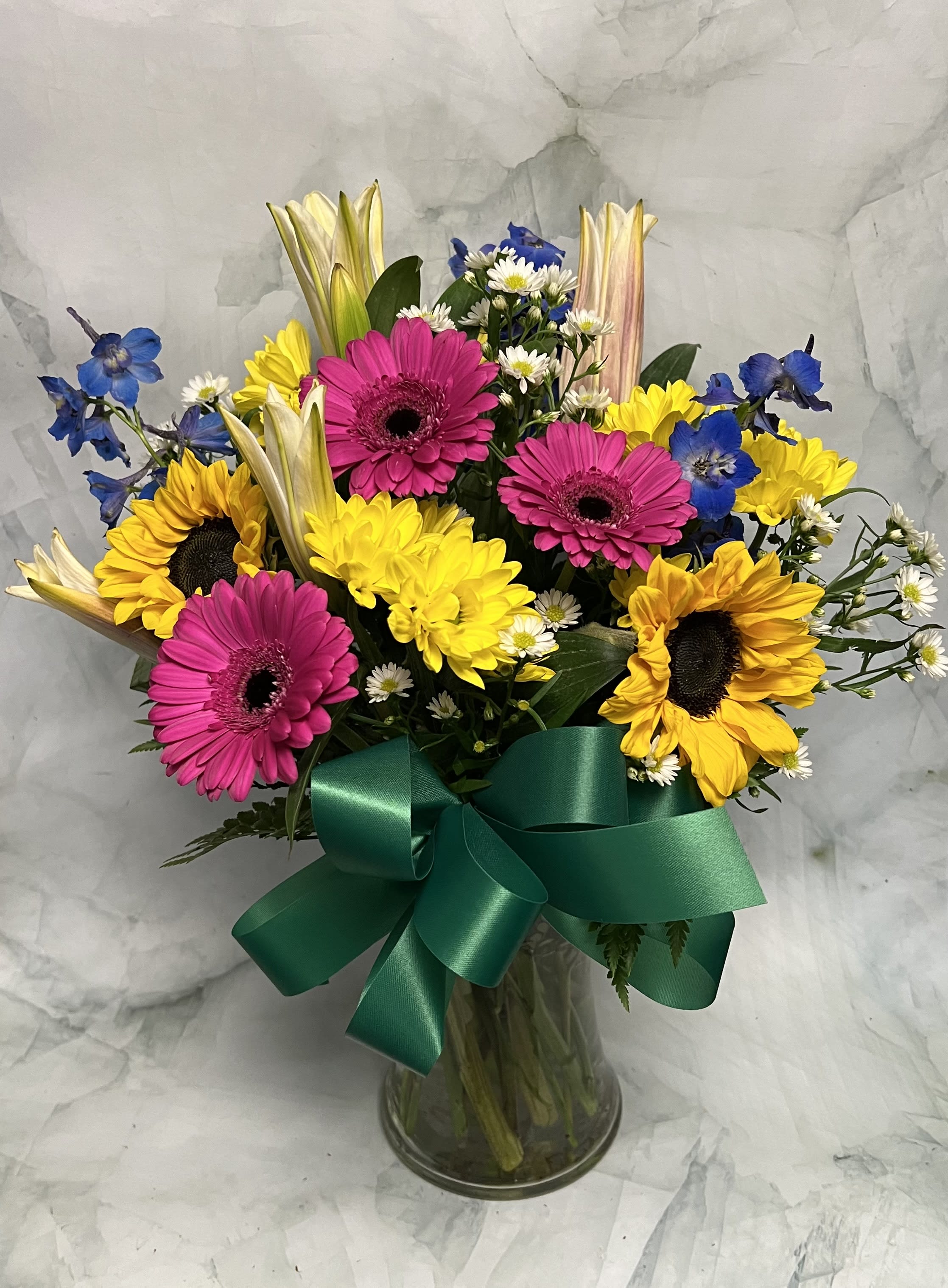 Bouquet of sunflowers, pink gerberas, and blue flowers in a glass vase